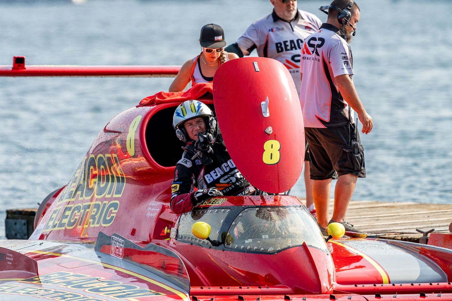Red hydroplane boat number 8 with Beacon Electric sponsorship prepares for race with crew members on dock.