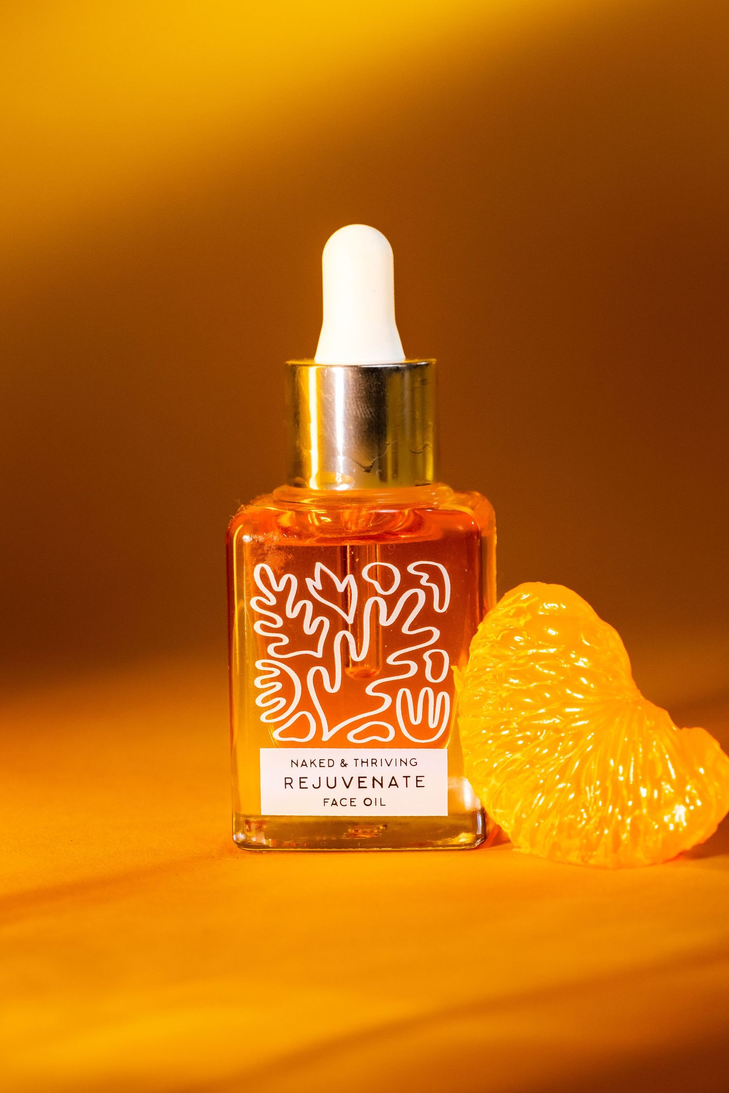 Naked & Thriving Rejuvenate Face Oil dropper bottle beside a citrus slice on a golden background.
