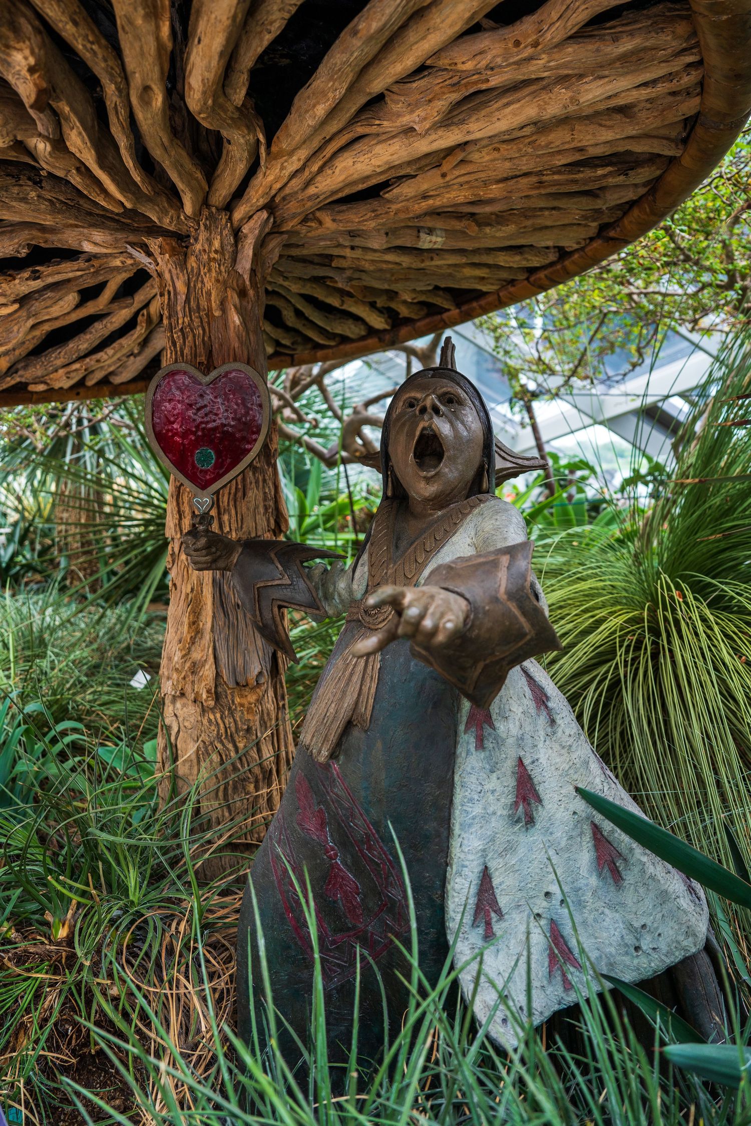 A dramatic bronze Queen of Hearts sculpture holding a heart under a giant mushroom.