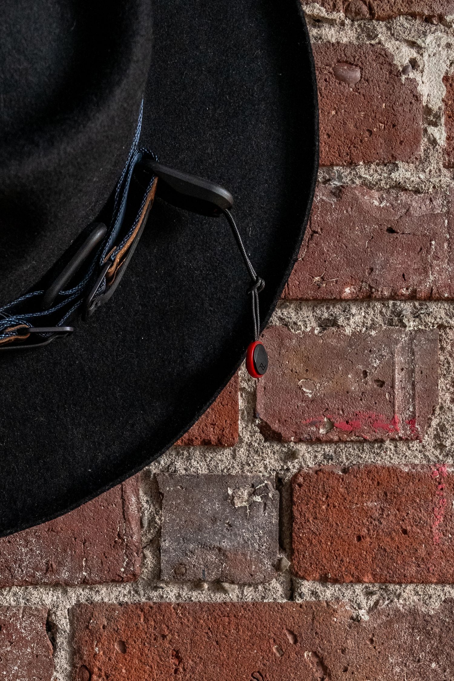 Black felt cowboy hat hanging on a rustic red brick wall with decorative band detail.