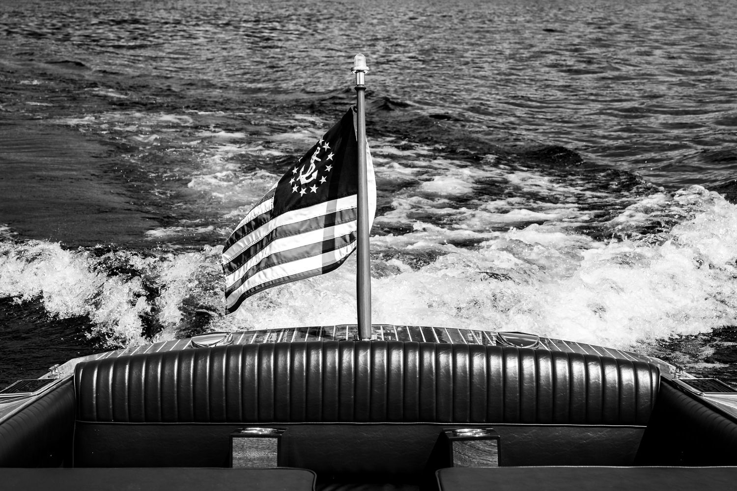 Black and white rear view of a classic wooden speedboat with an American flag cutting through water.