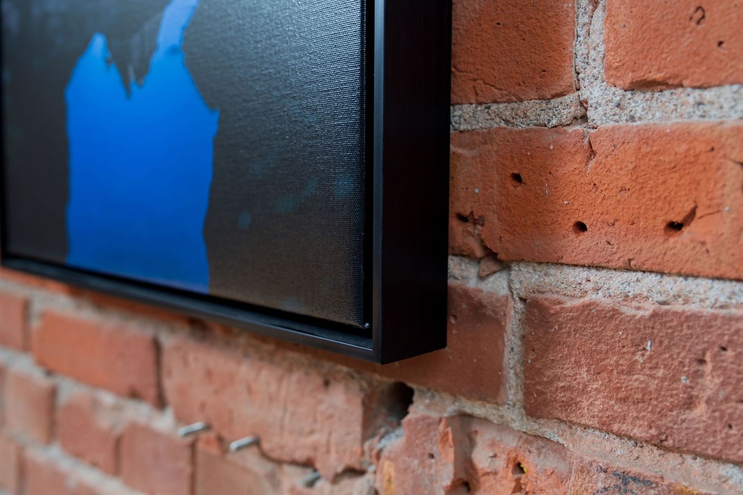A framed blue abstract artwork mounted on a rustic red brick wall, showcasing modern art display.