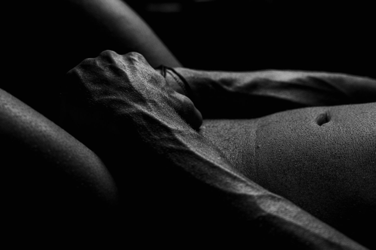 Close-up black and white artistic photo of a hand resting on a human torso in dramatic low-key lighting.