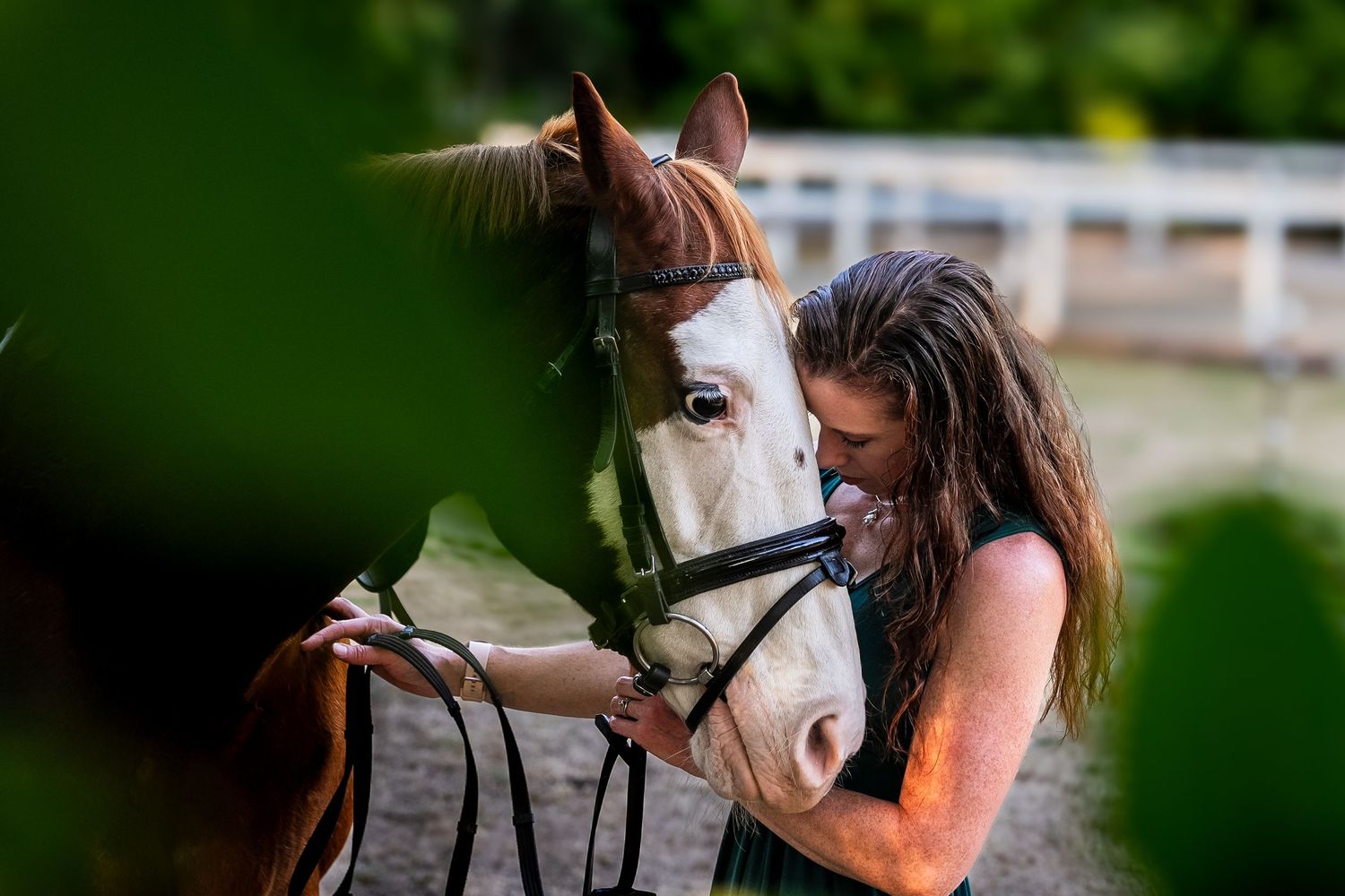 A young woman tenderly holding the bridle of a chestnut and white horse outdoors.