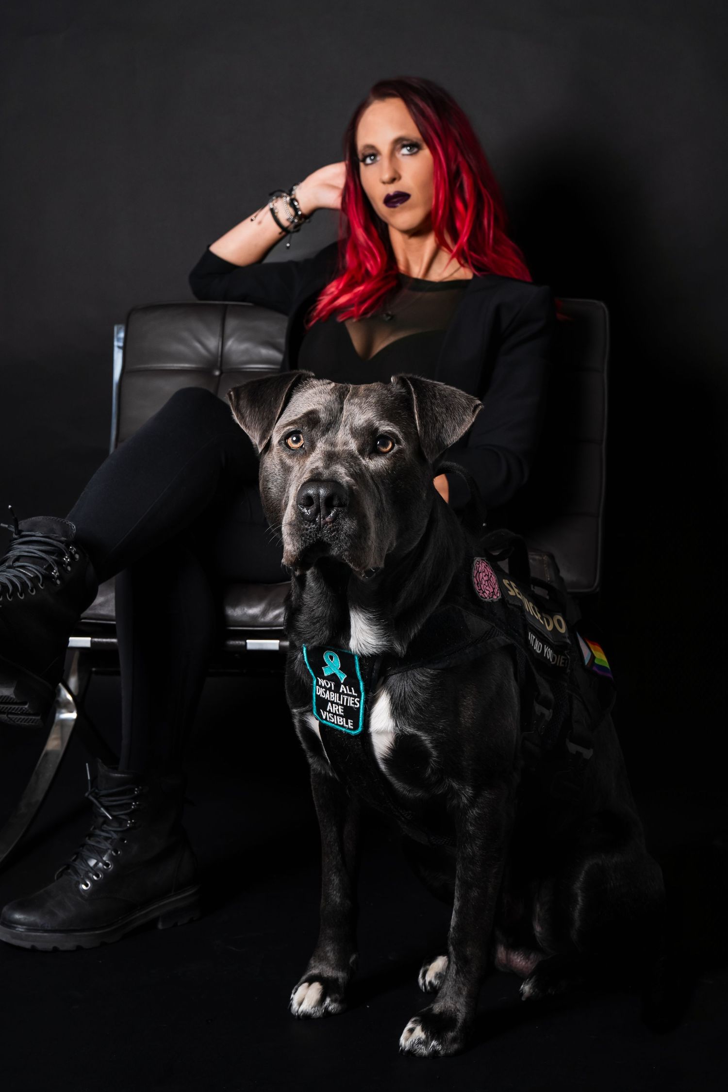 Red-haired woman in black outfit posing with a large gray Cane Corso service dog in studio.
