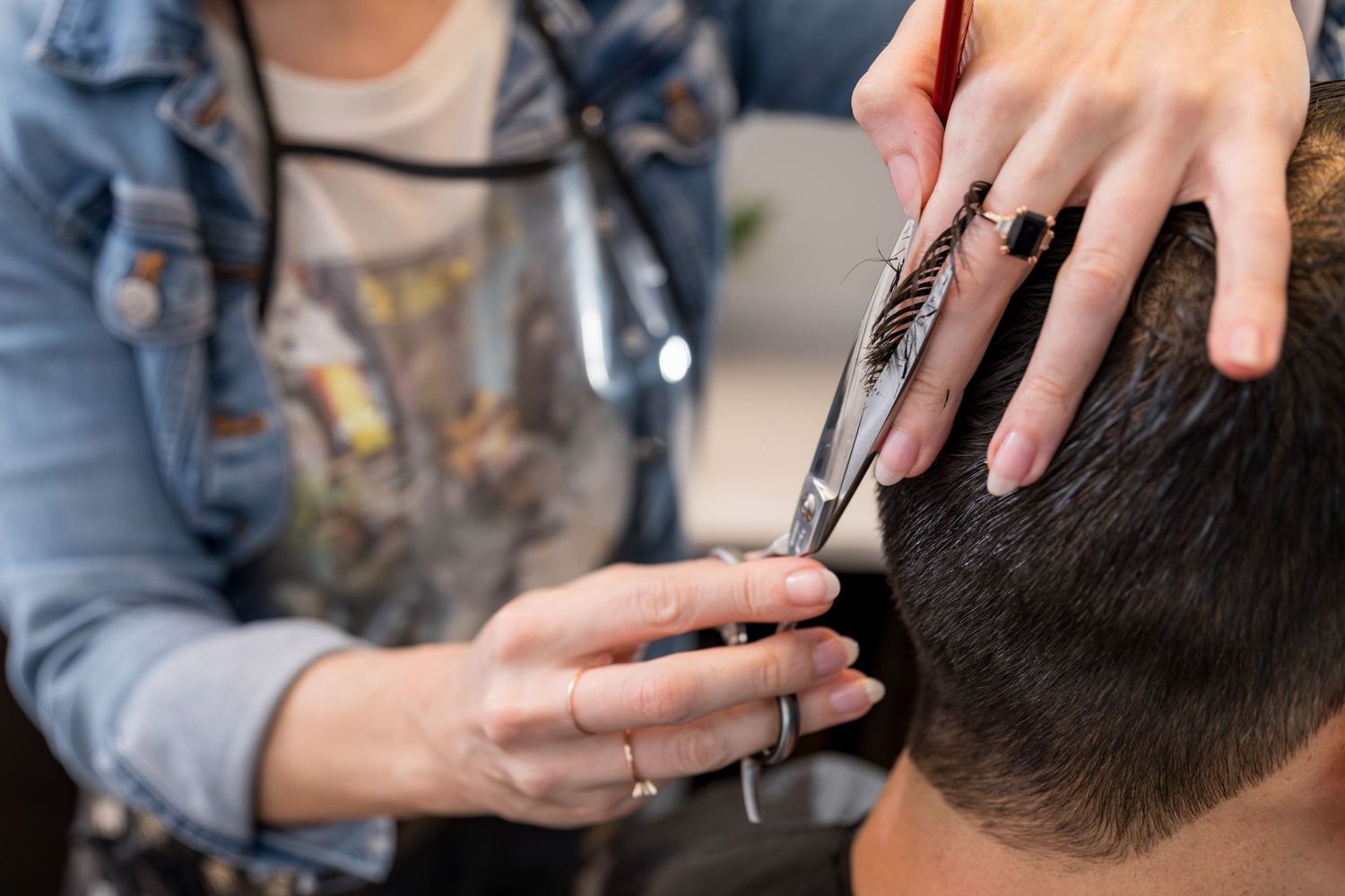 Hairstylist cutting dark hair with scissors in a barbershop.
