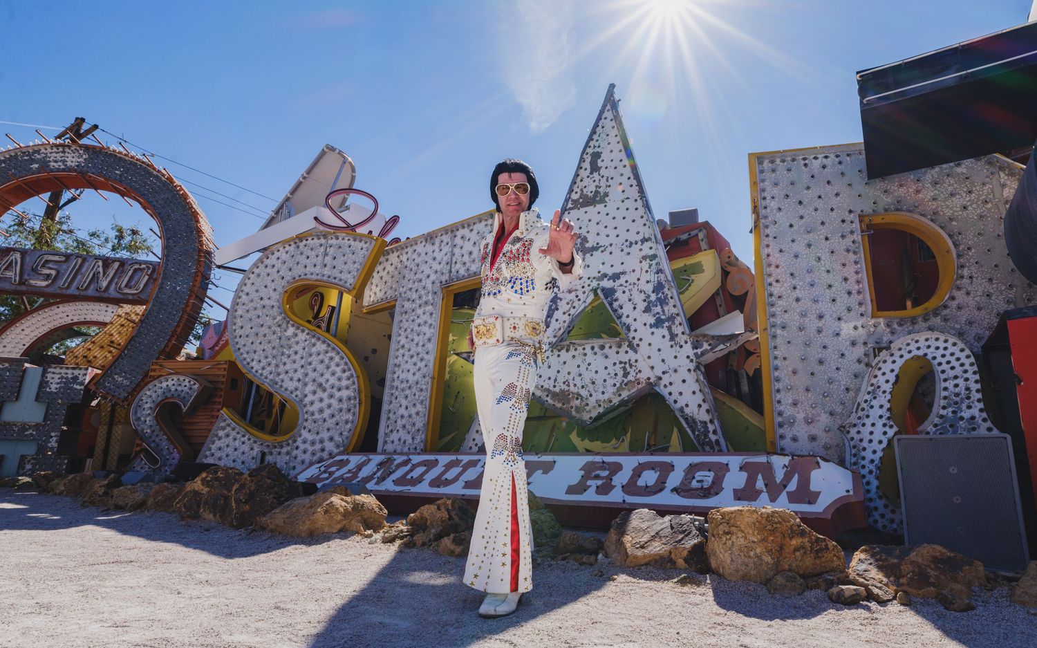Elvis Presley impersonator posing in white rhinestone jumpsuit at the Las Vegas Neon Museum.