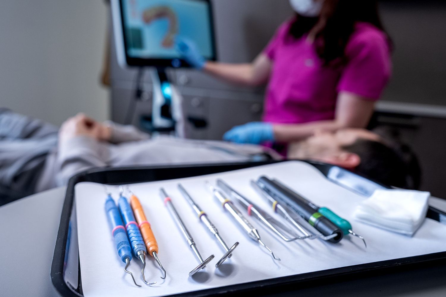 Dental hygienist preparing sterile instruments on a tray during a patient examination procedure.