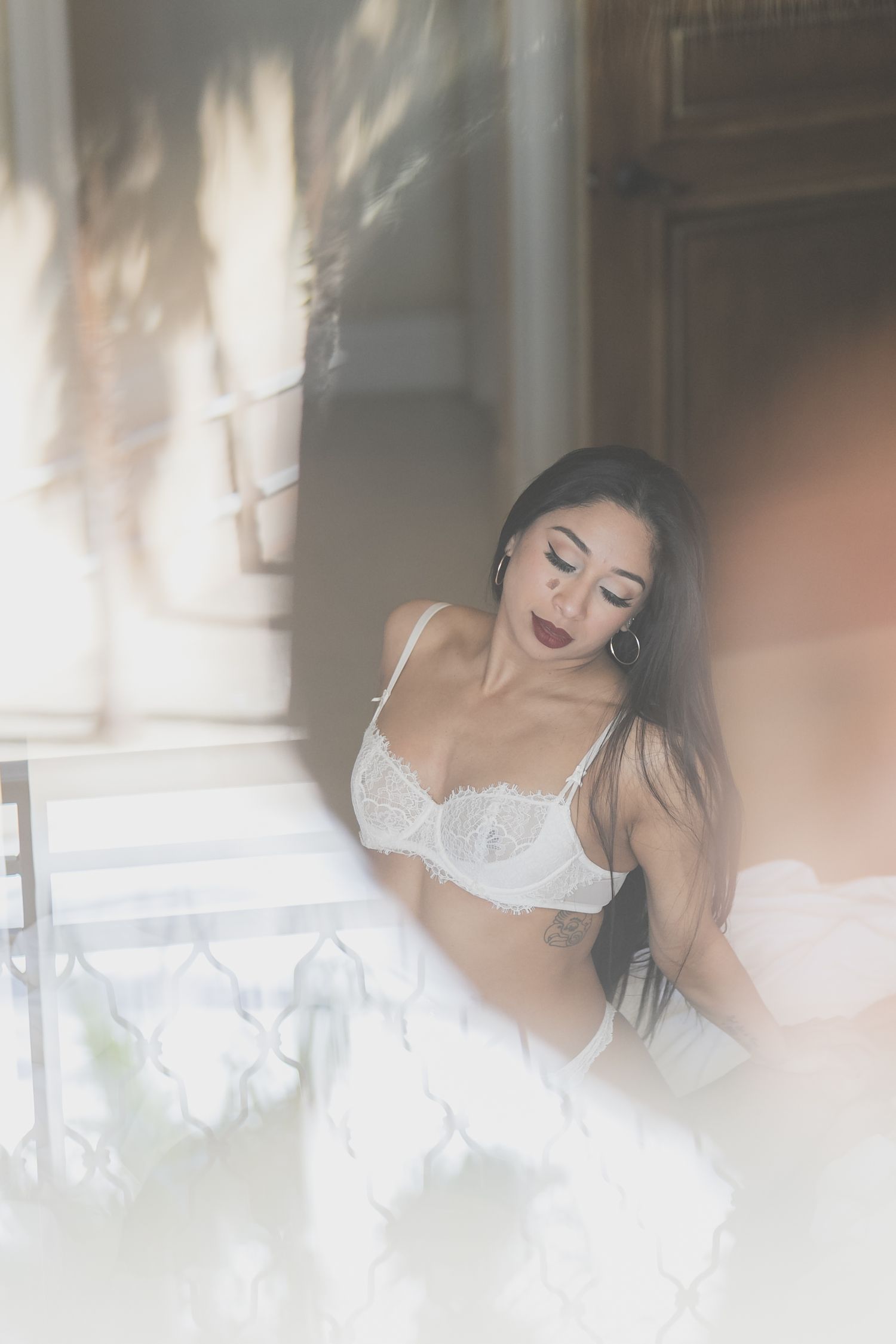 Woman in white lace lingerie posing elegantly near a bright window with soft natural light.