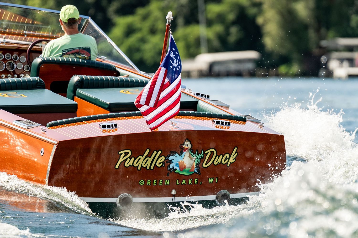 Vintage wooden speedboat named Puddle Duck from Green Lake WI with American flag speeding across water.