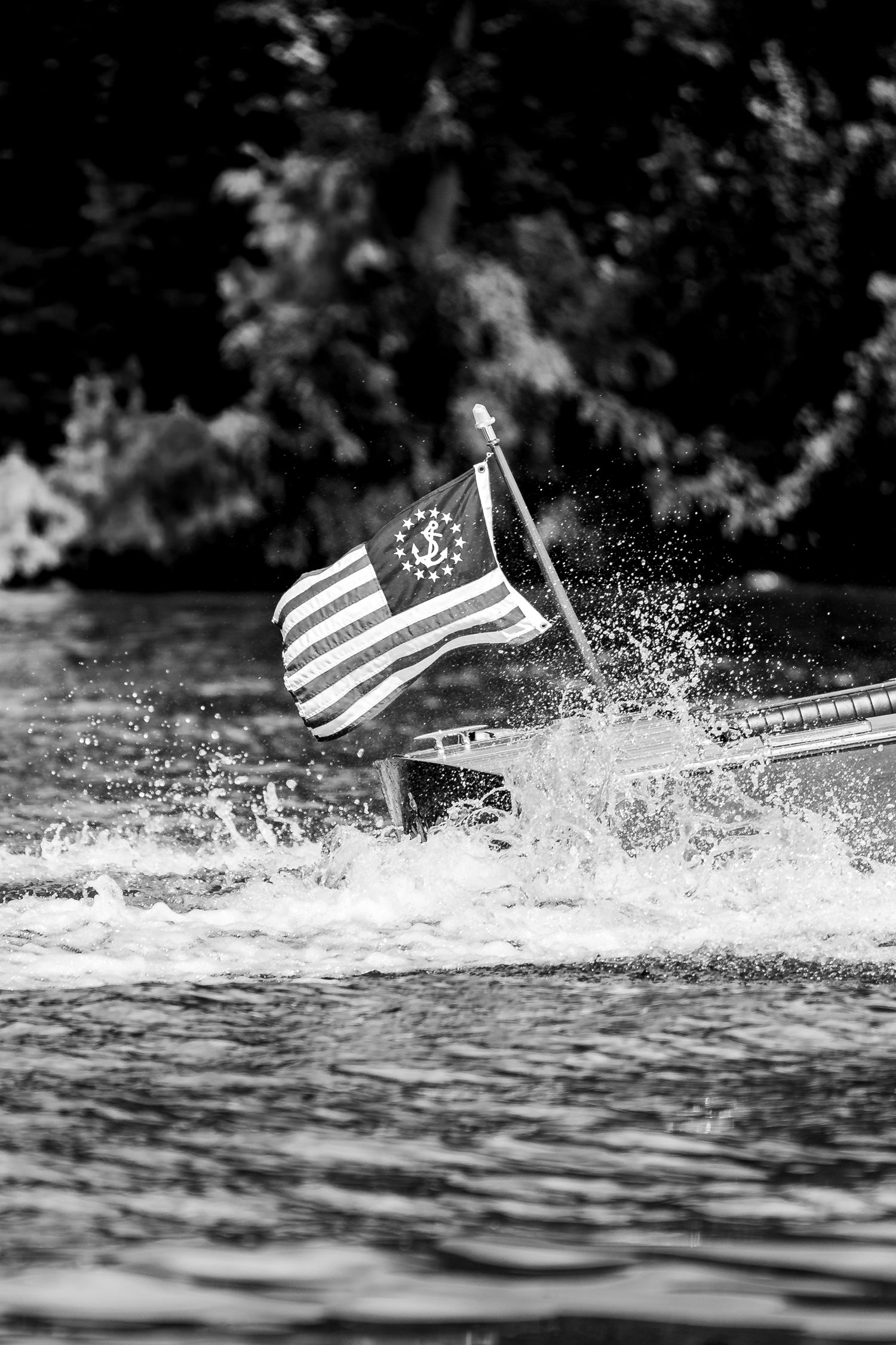 Black and white photo of an American Yacht Ensign flag on a speedboat stern with water spray.