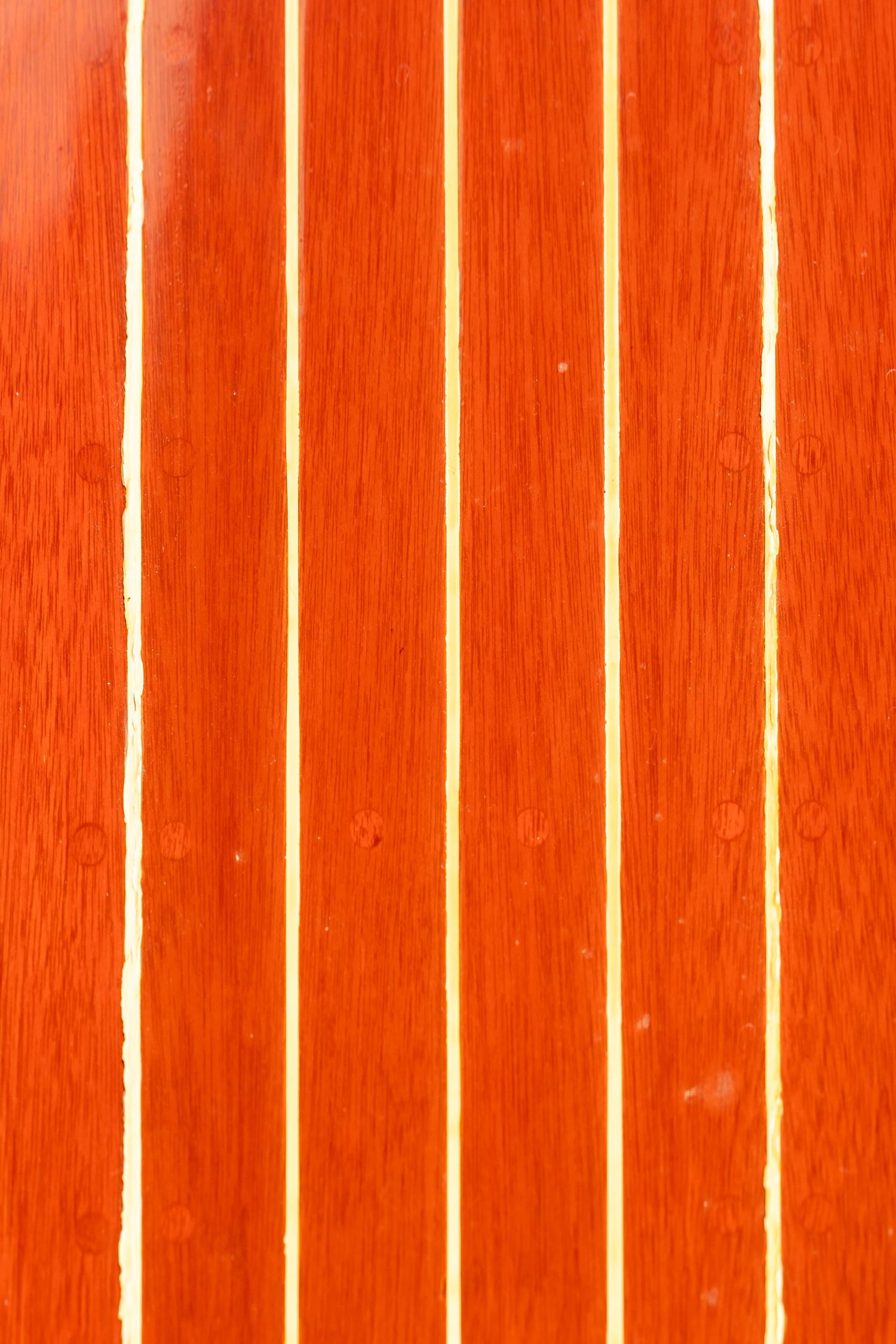 Close-up of varnished mahogany wooden boat deck planks with white caulking seams between boards.