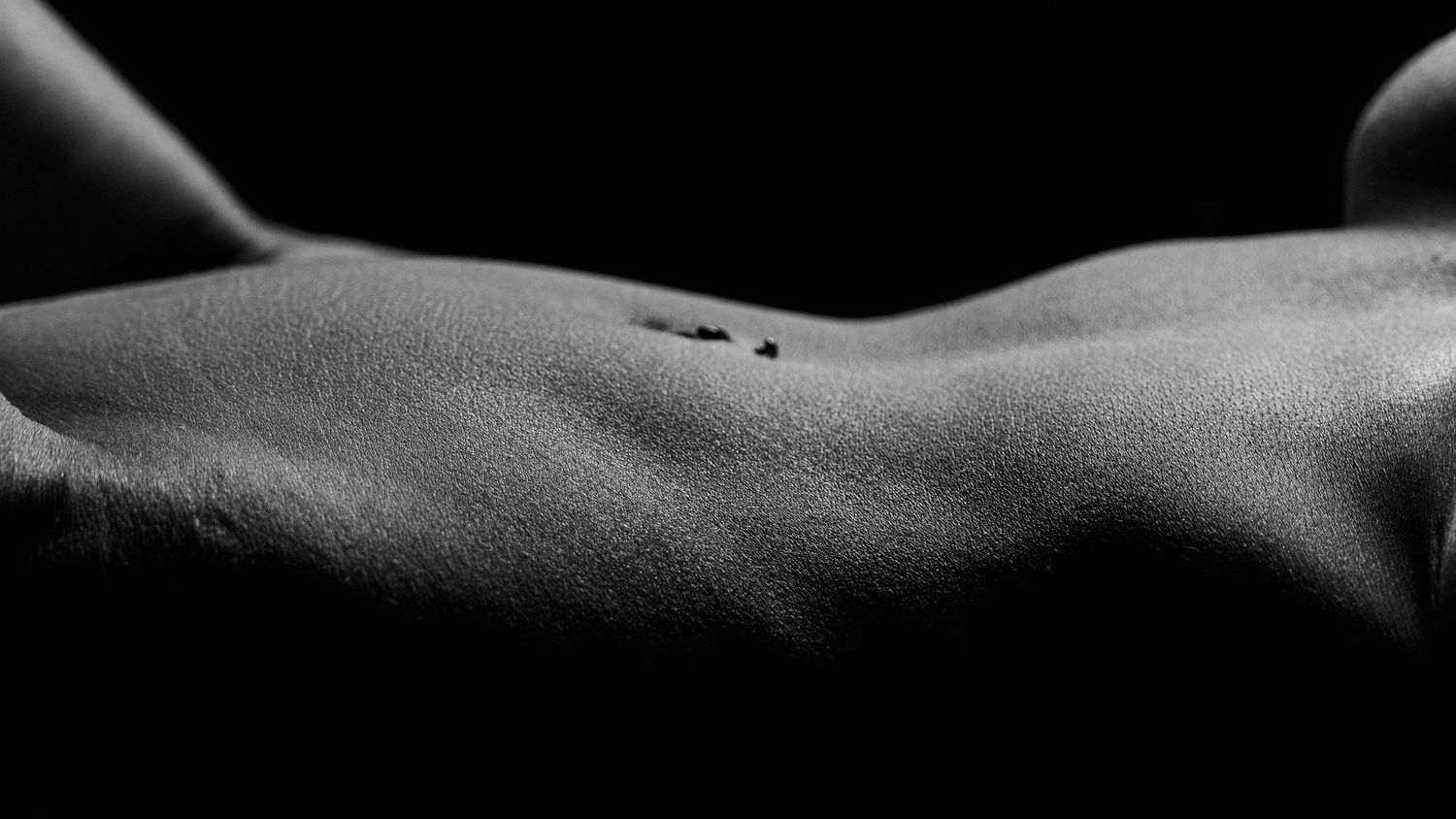 Black and white artistic photo of a human back with small tattoos, dramatic lighting highlighting skin texture.
