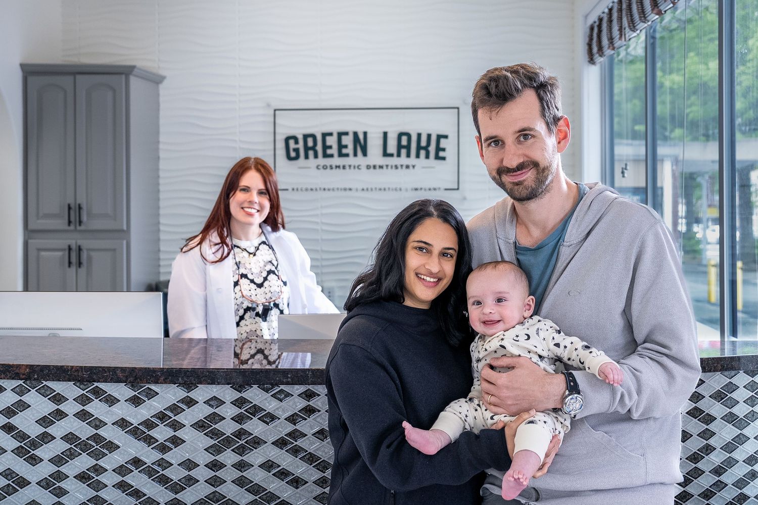 Happy family with baby smiling at Green Lake Cosmetic Dentistry reception desk.
