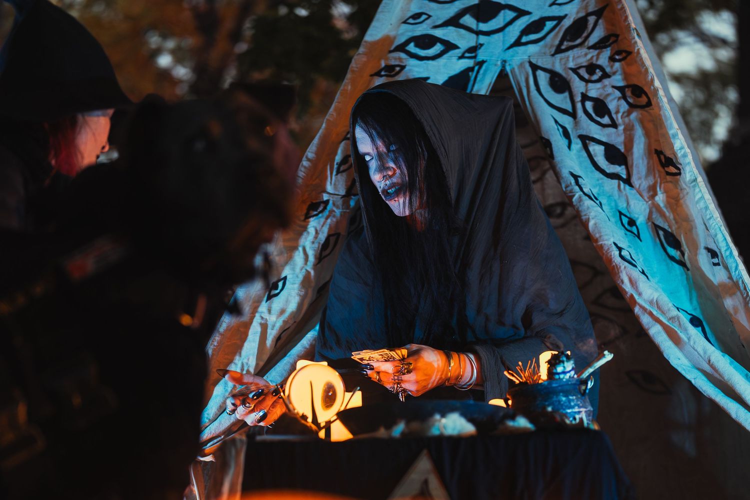 A performer in dark robes and dramatic makeup reaches forward aggressively at a nighttime Halloween event.