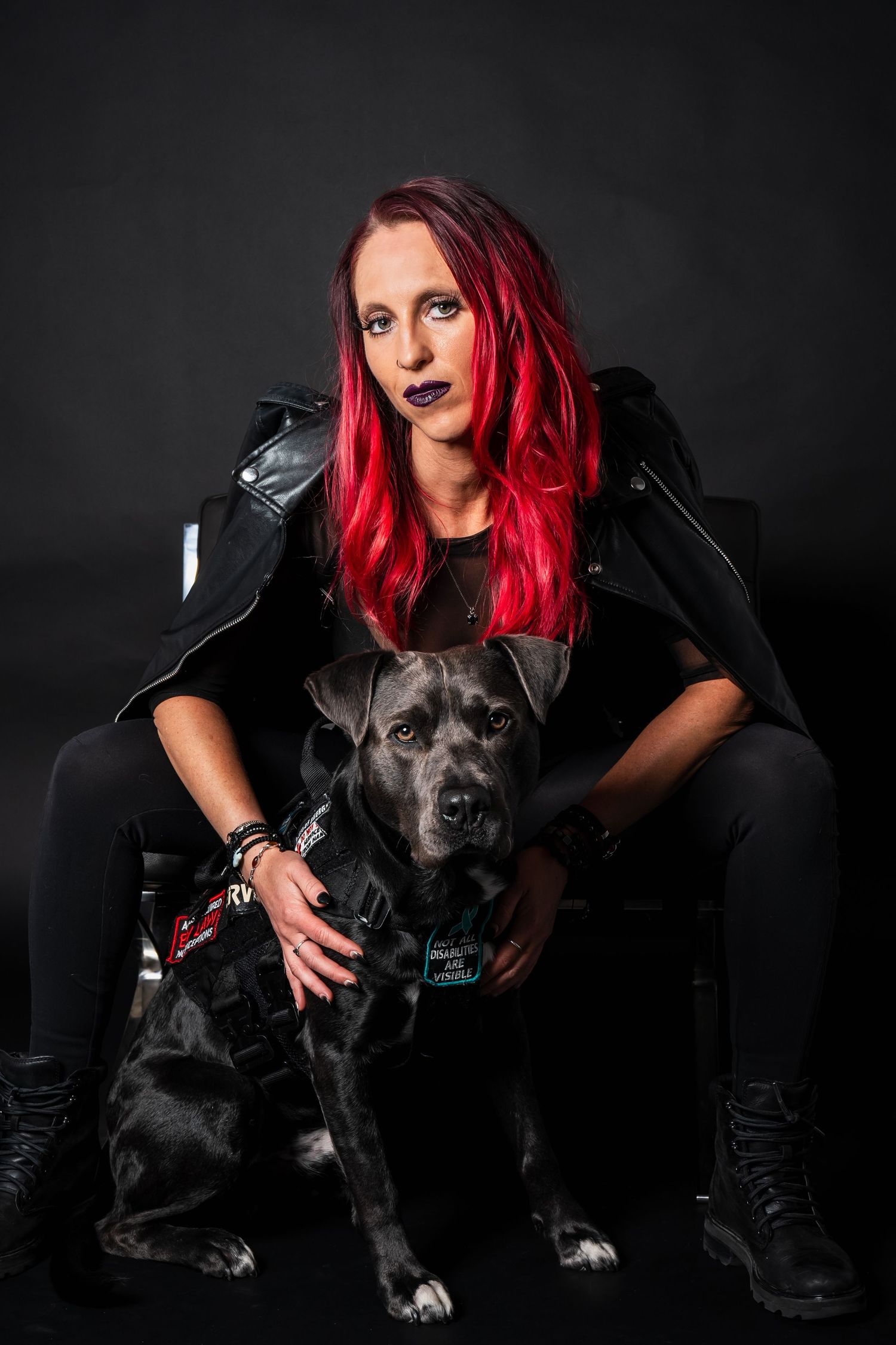 A red-haired woman in black outfit poses with her gray Cane Corso service dog.