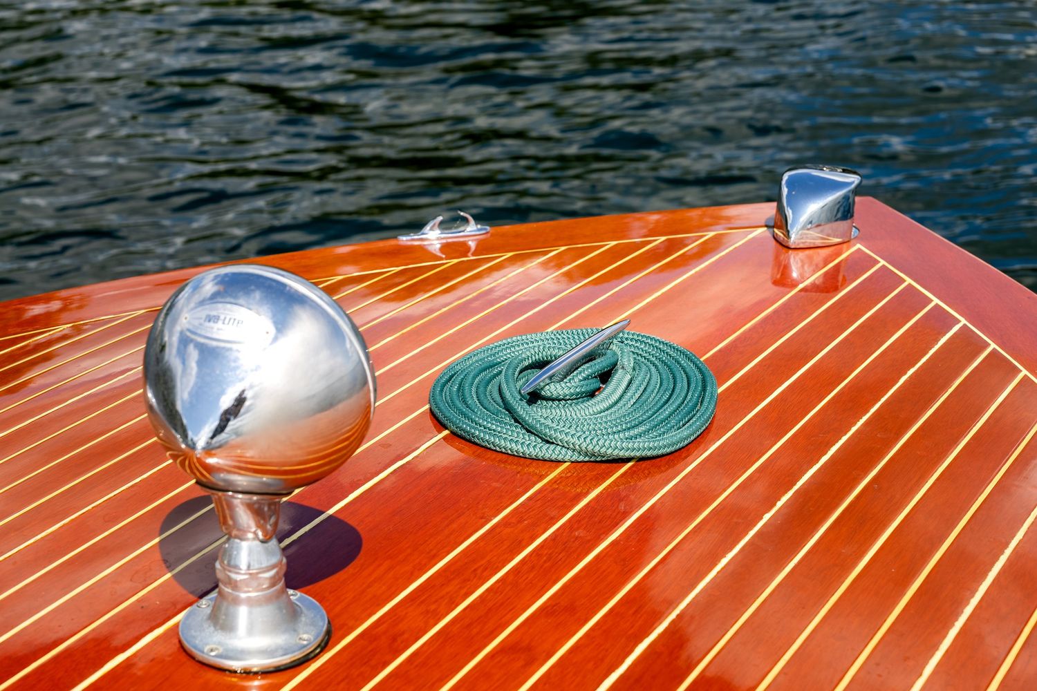 Close-up of a polished chrome ball ornament and coiled green rope on a classic wooden boat deck.