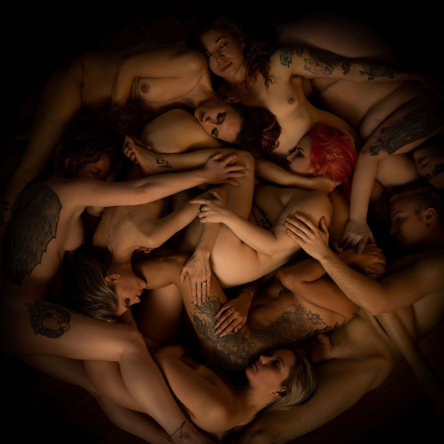 Artistic overhead view of multiple nude figures intertwined together in warm dramatic lighting.