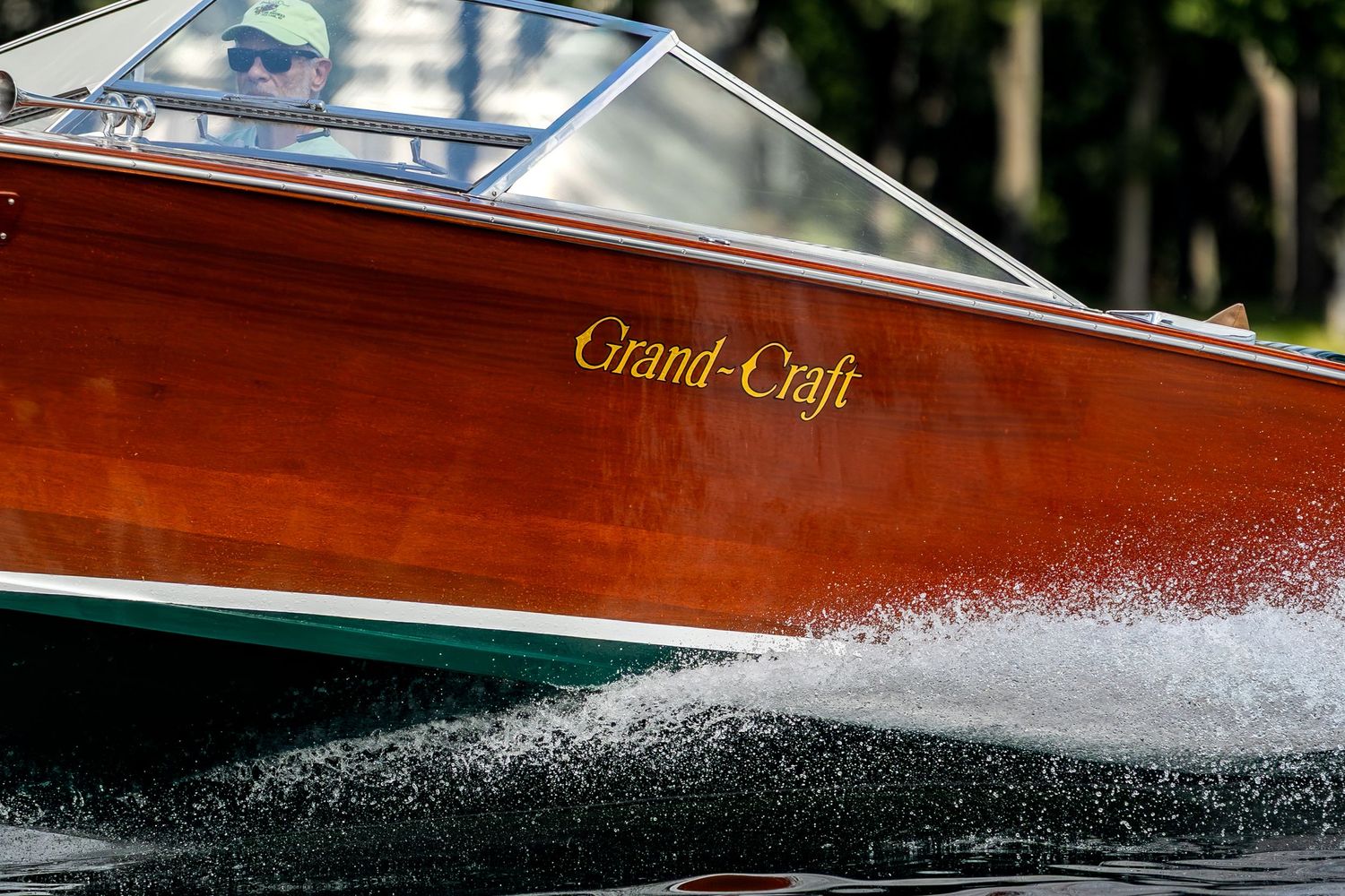 A classic Grand-Craft wooden speedboat cutting through water at high speed, creating a dramatic white spray wake.