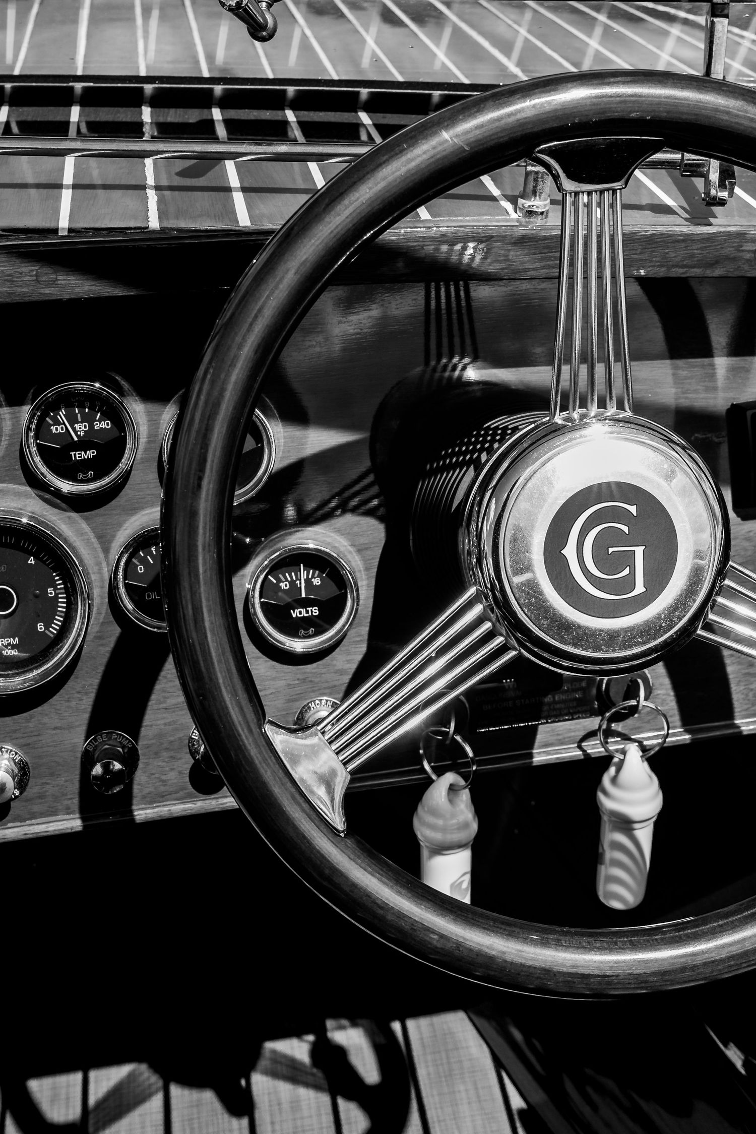 Black and white vintage boat interior showing classic steering wheel with G logo and dashboard gauges.