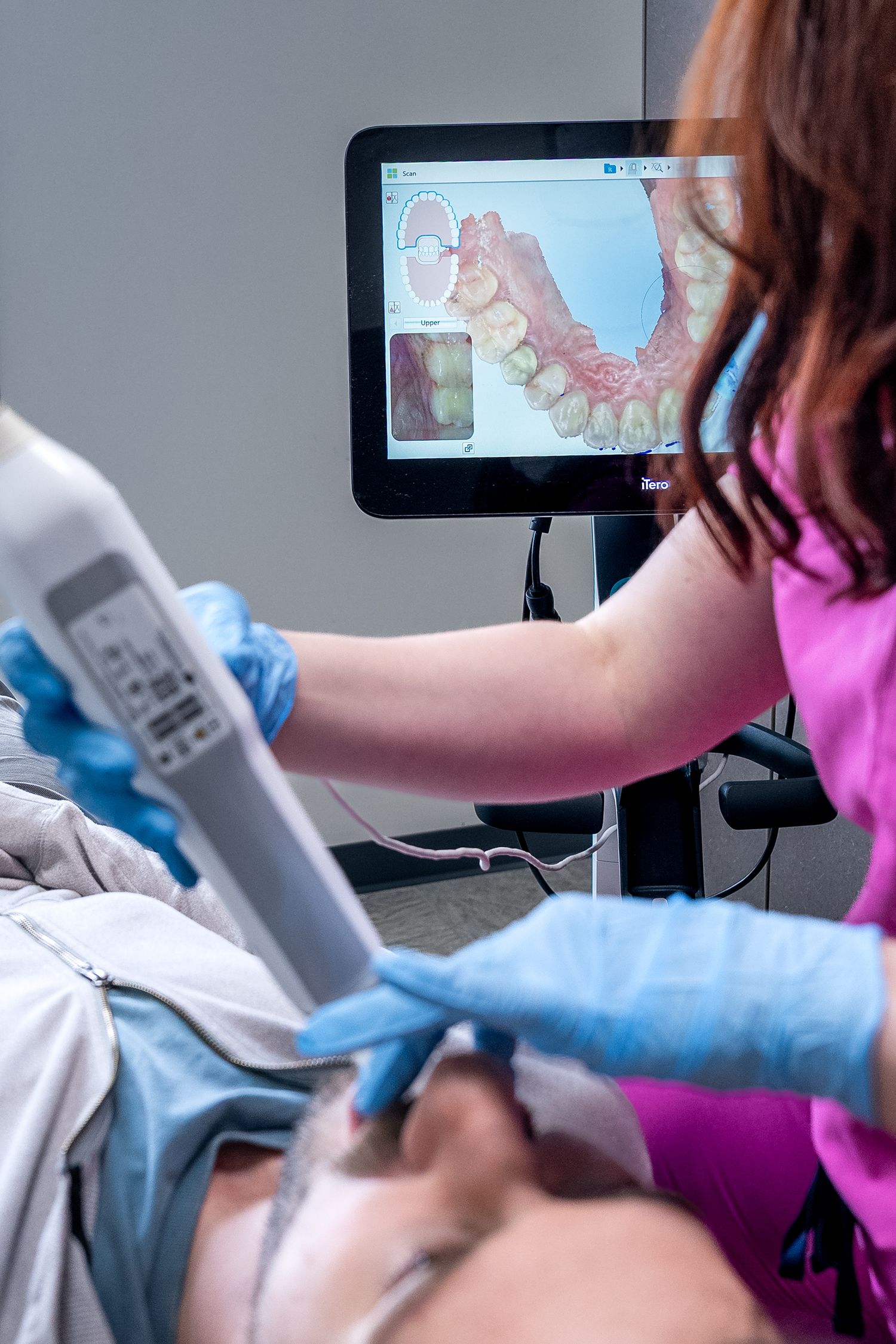 Dentist using intraoral scanner on patient with 3D tooth scan displayed on monitor in dental office.