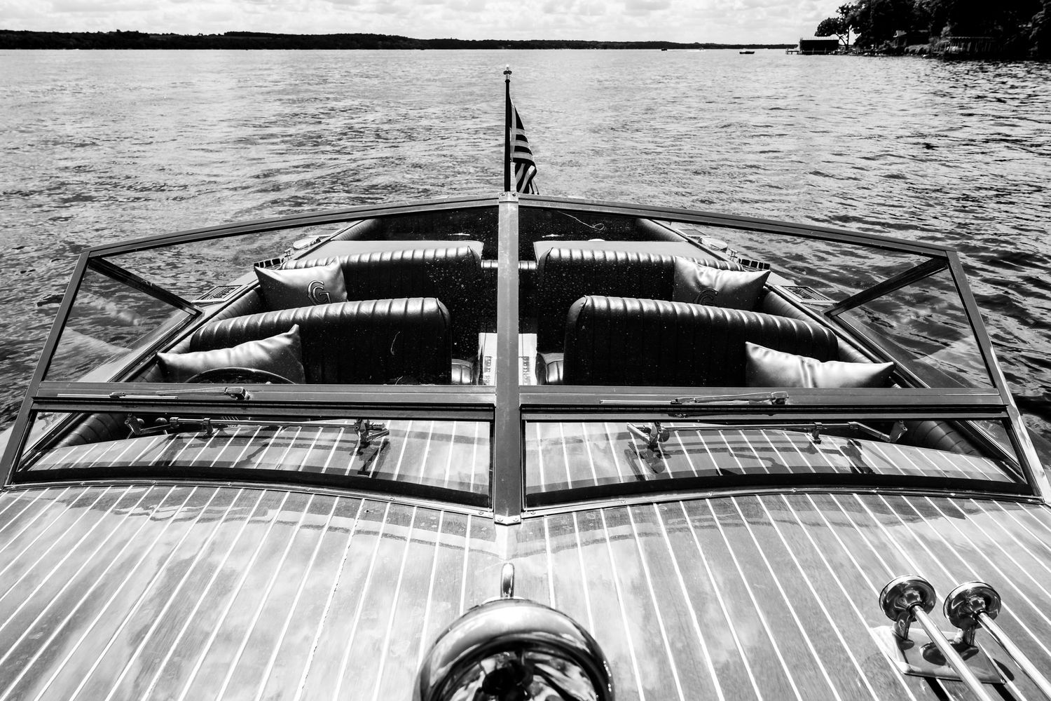 Black and white aerial view of classic wooden boat deck with tufted seating and American flag at stern.