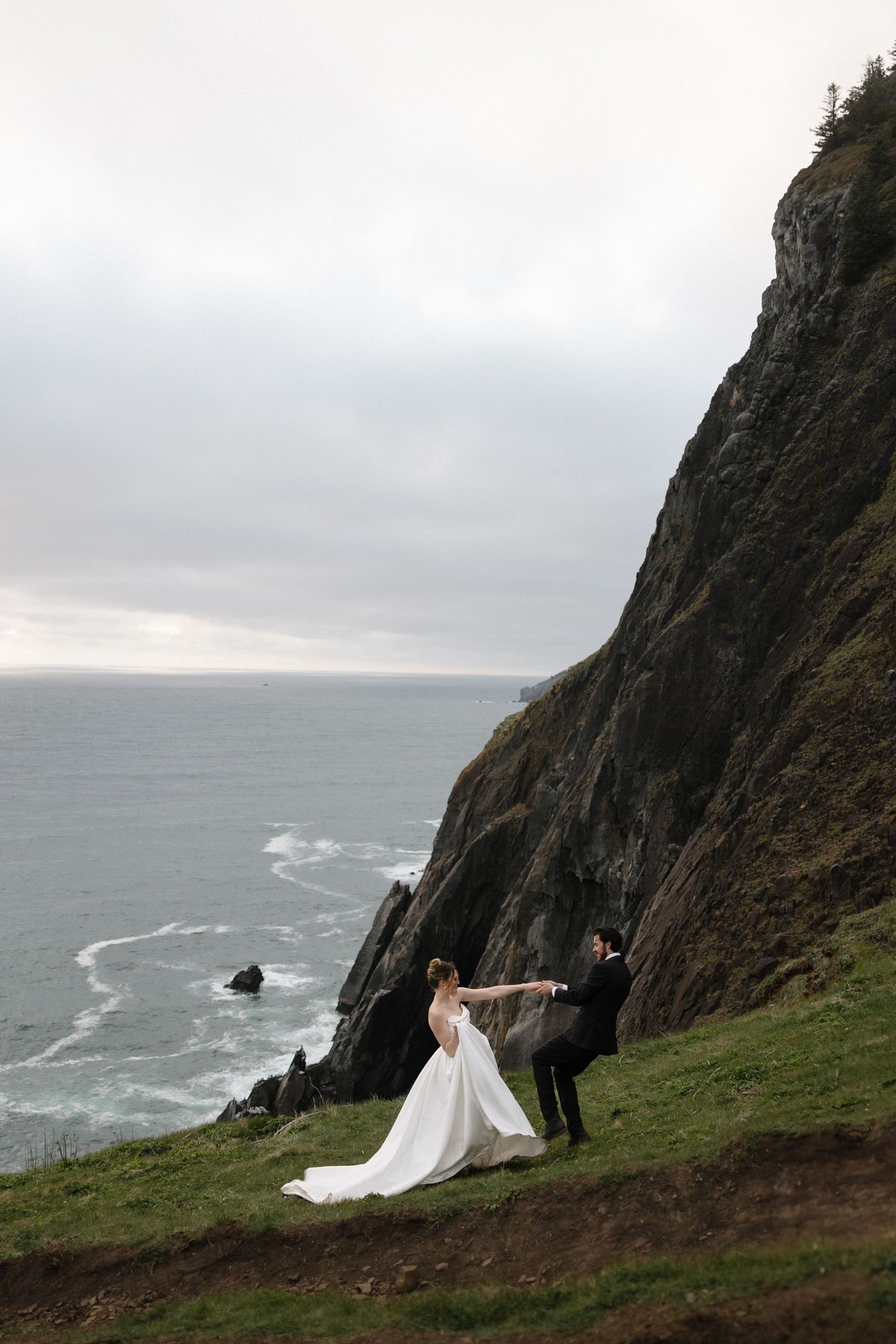 Dramatic coastal wedding photos on cliff edge overlooking stormy ocean.