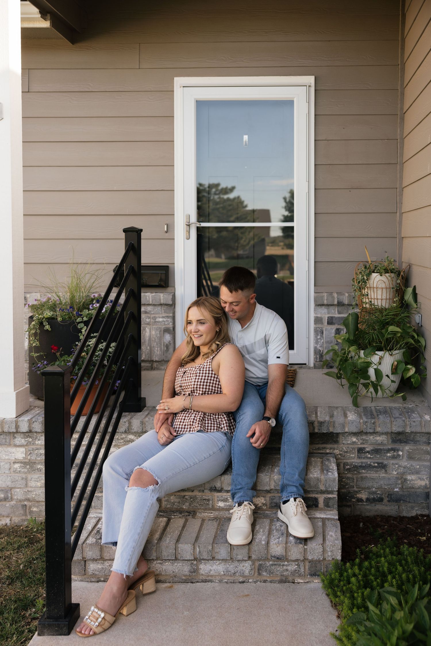 Couple sitting together on brick front porch steps of a home, smiling and embracing on a sunny day.
