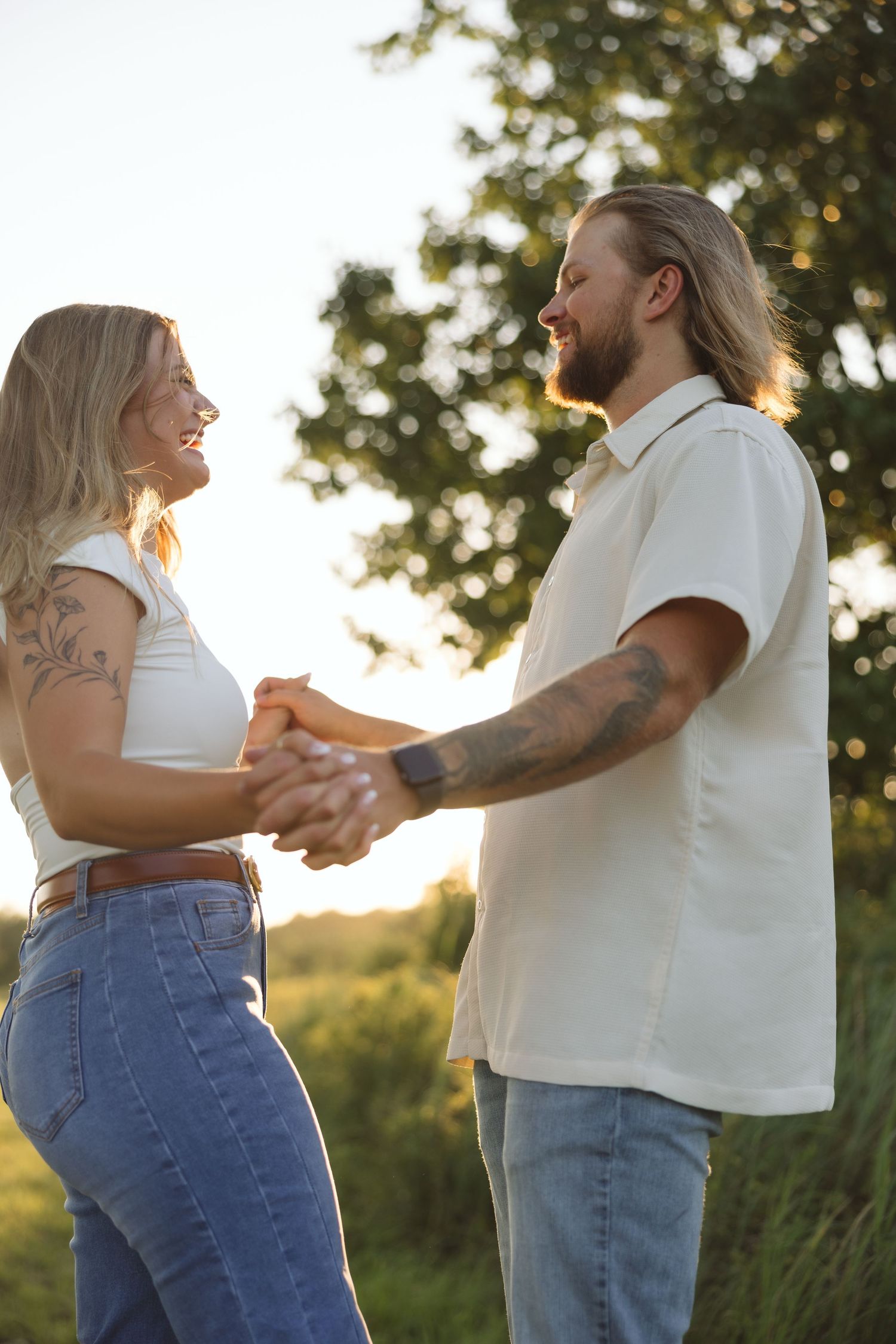 A couple dances in casual attire during golden hour in a summer field.