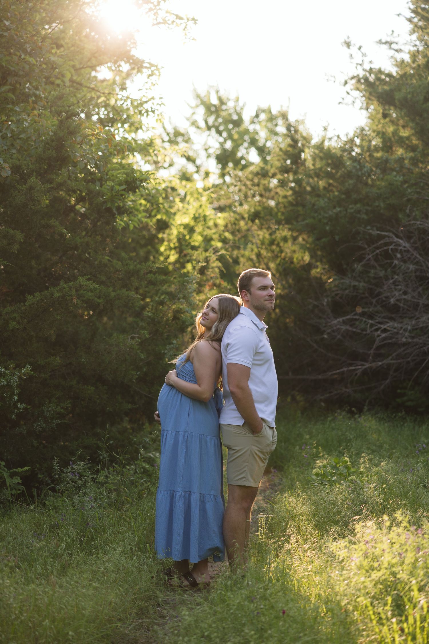 A couple poses in a sunlit meadow during golden hour.