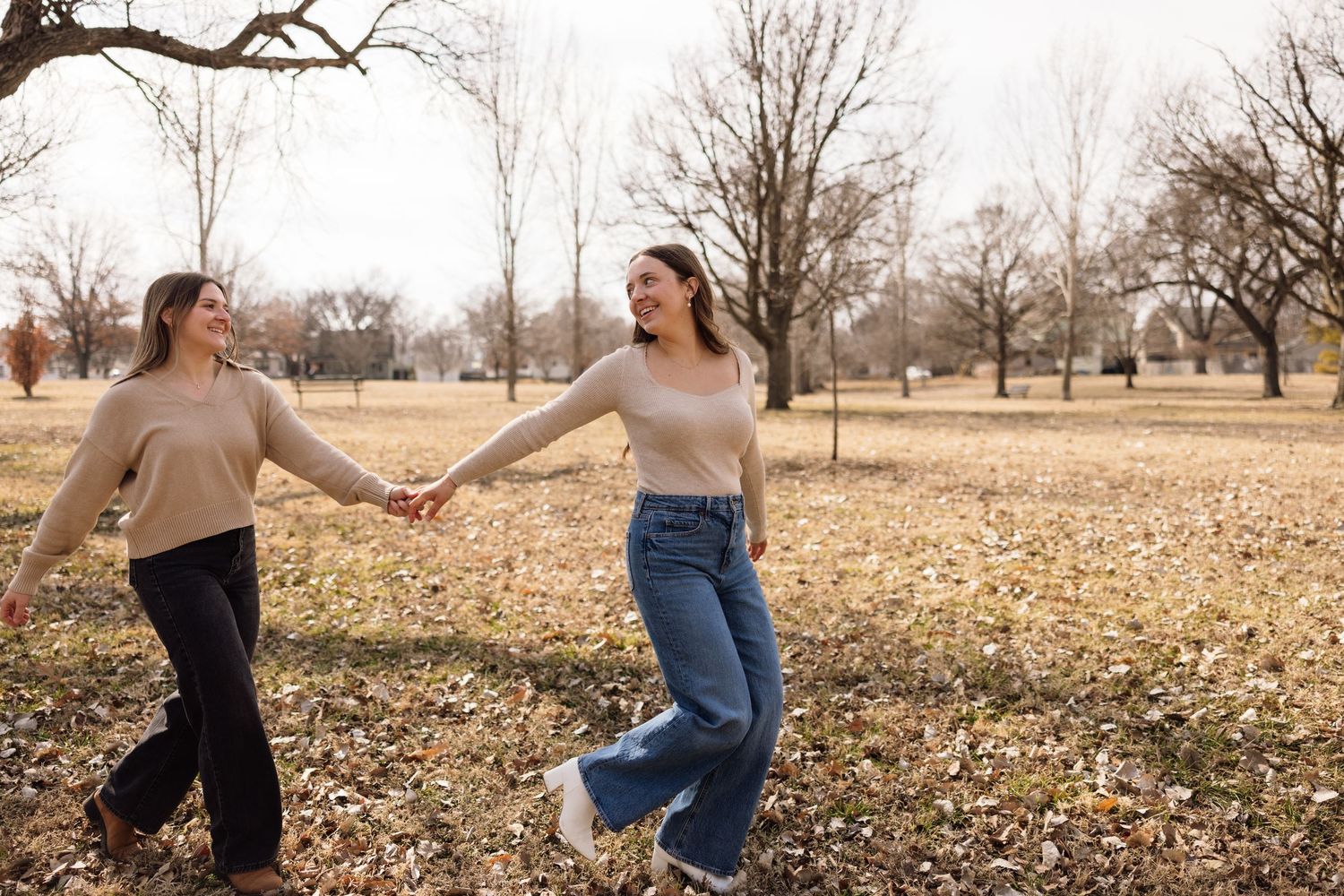 Playful couple enjoying autumn leaves in a park during golden hour.