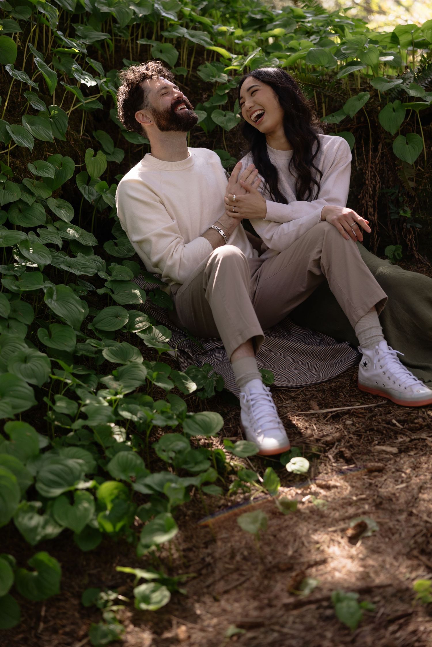 Couple sitting among green foliage sharing joyful laughter together.