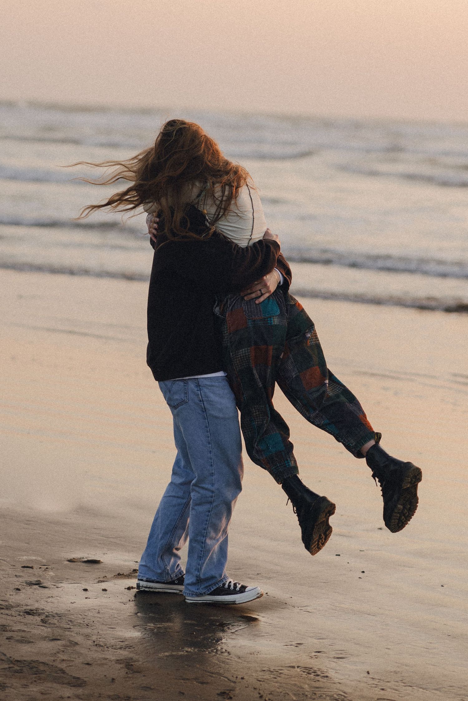 Playful figures dance and spin on a beach at sunset.