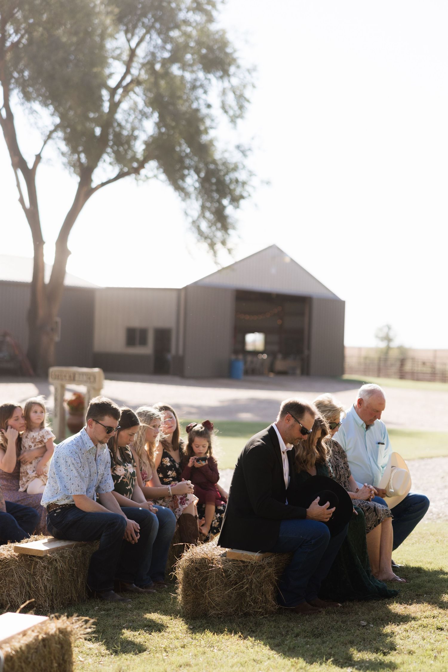 Wedding guests relaxing on hay bales during outdoor country celebration.