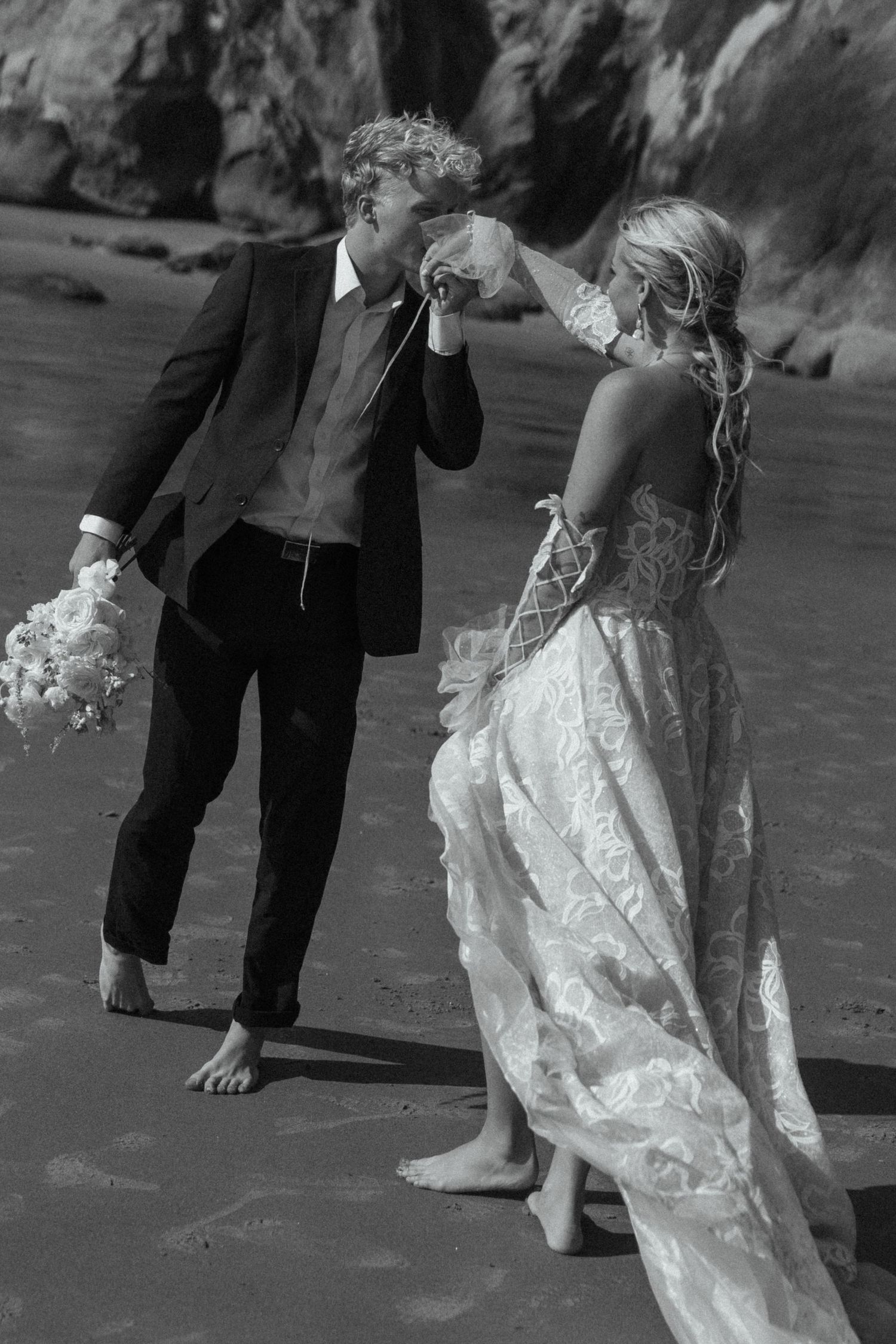 Black and white photo of couple dancing barefoot on beach in formal attire.