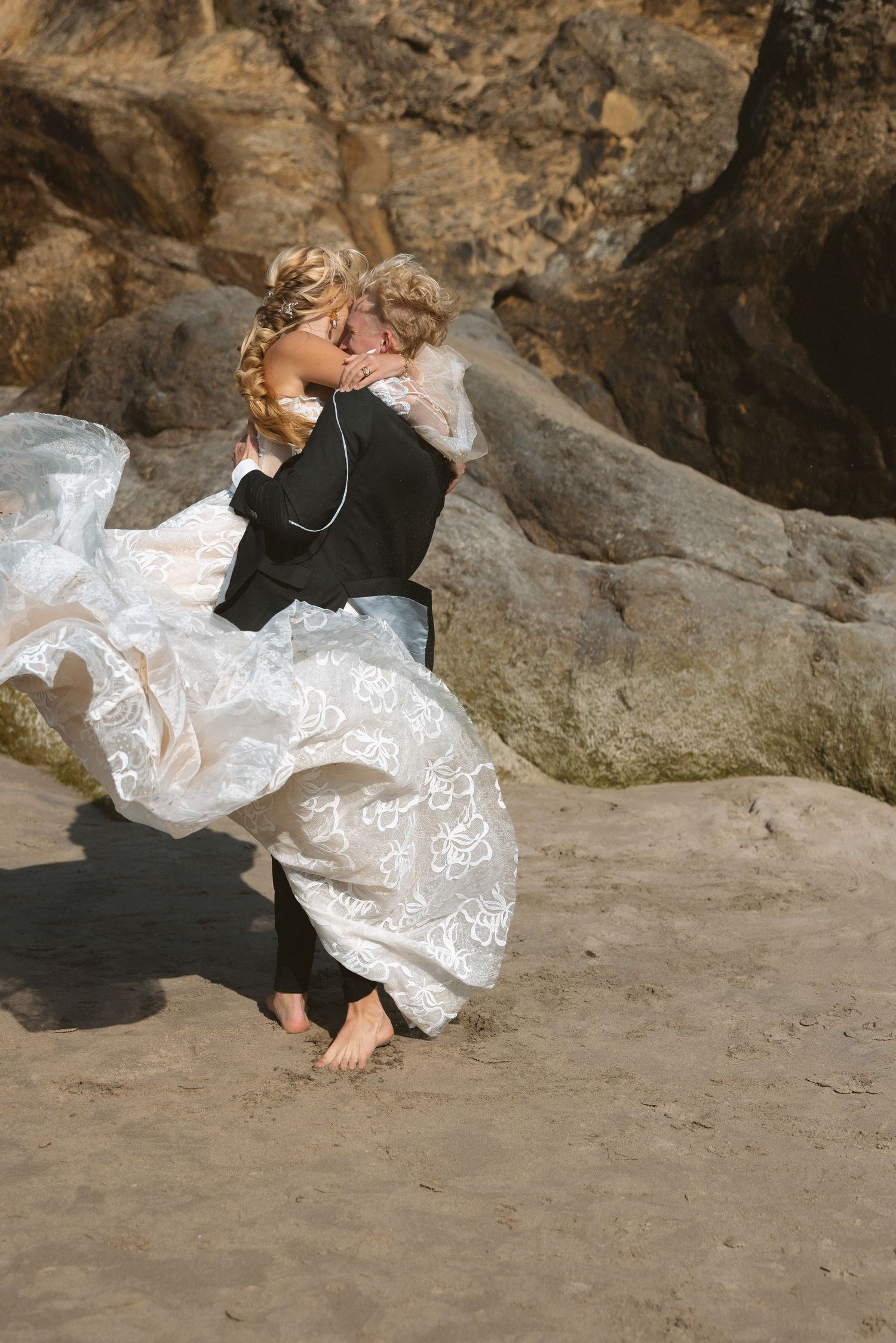 Wedding couple posing on sandy beach near rocky cliffs.