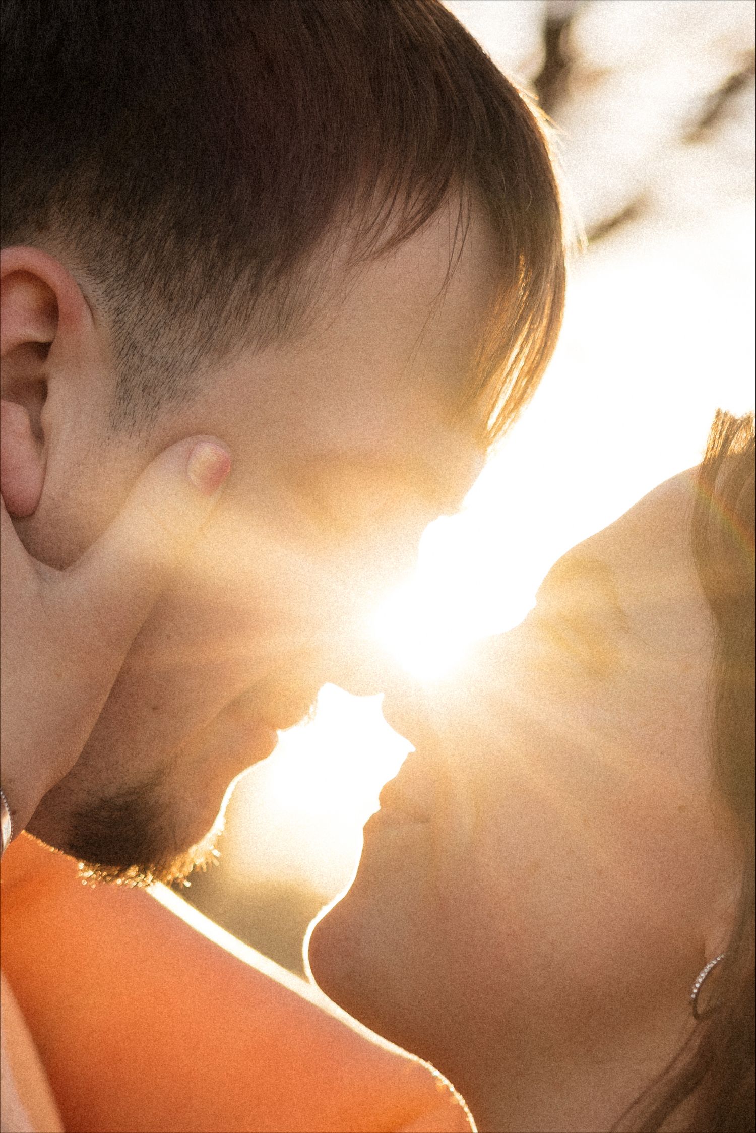 A romantic silhouette of a couple kissing in warm golden sunlight with lens flare creating a dreamy atmosphere.