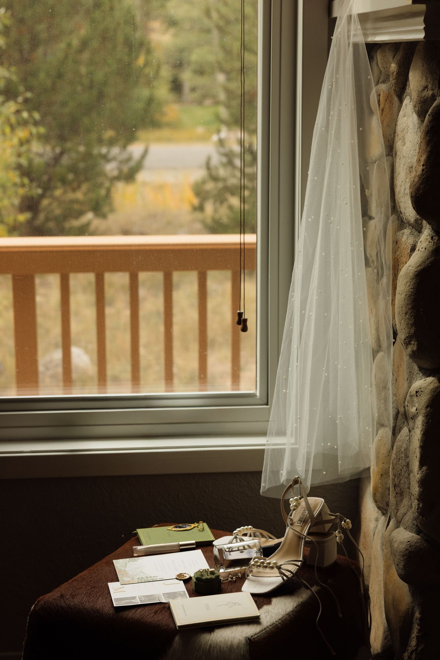 Bridal veil and heels on a table by a window with a wooden deck view, wedding day preparations.