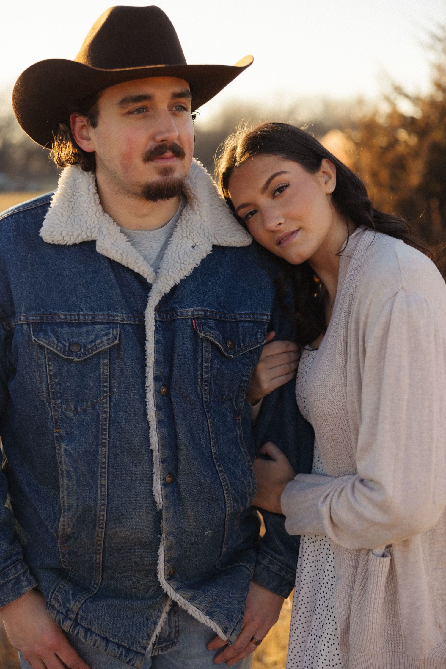 Romantic couple in western wear embracing during a golden sunset photoshoot.