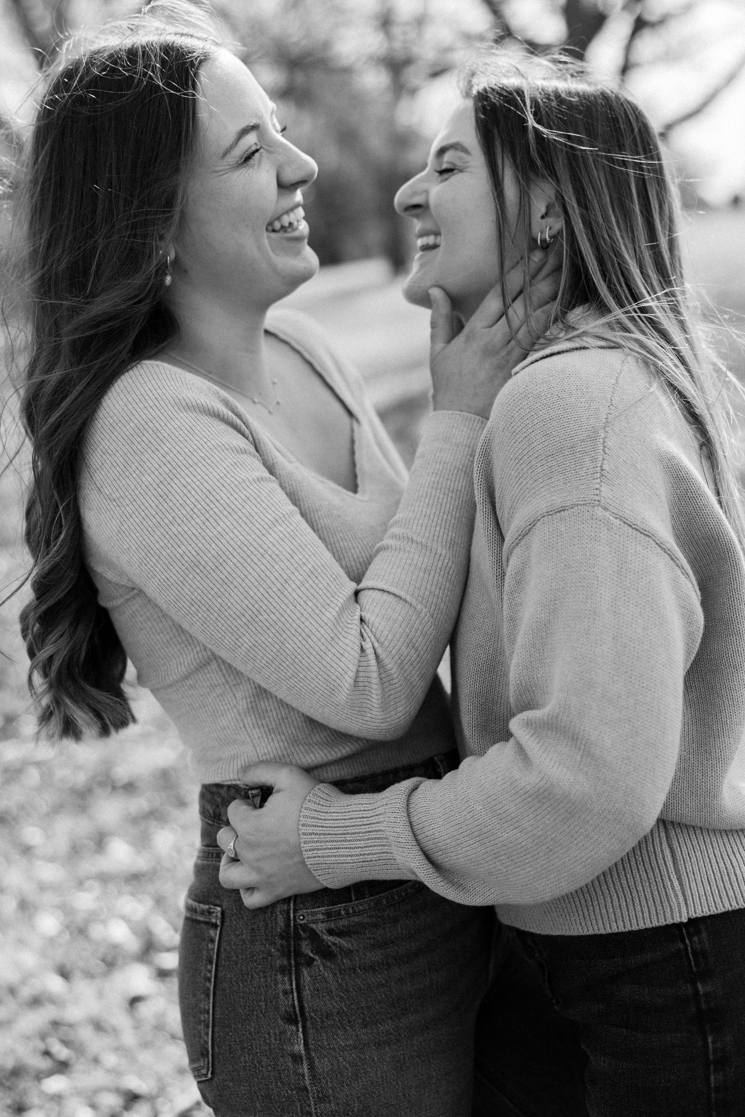 Two people in sweaters share joyful laughter in black and white photography.