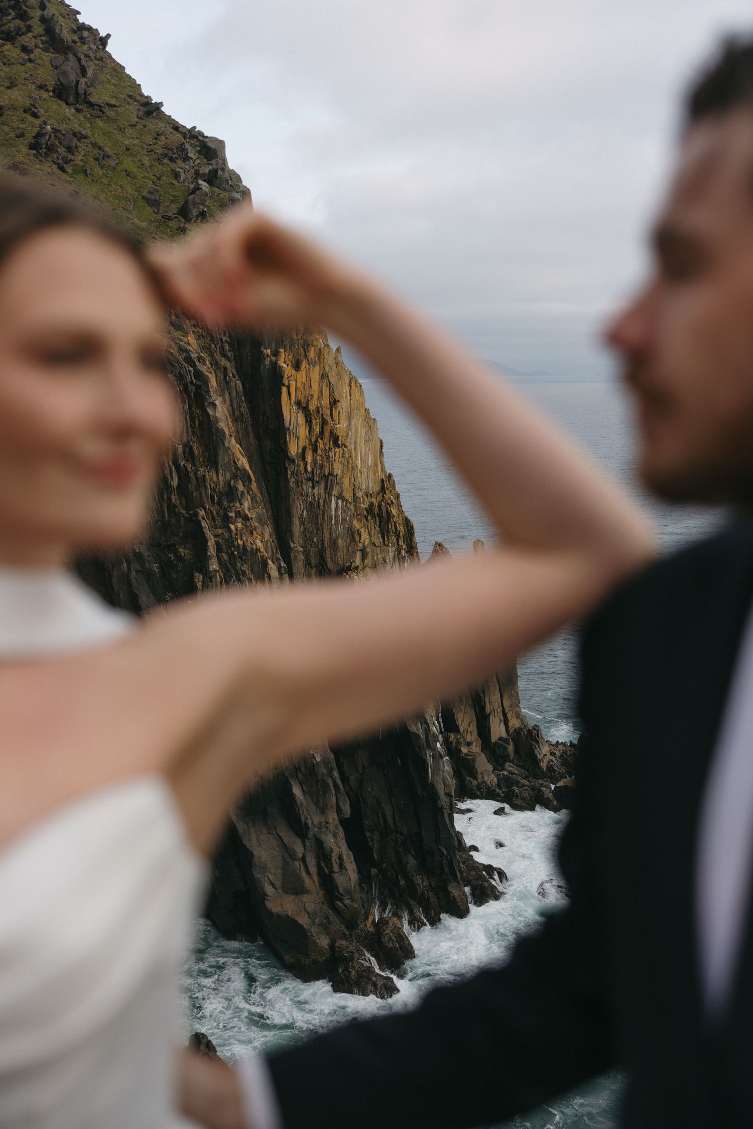 Dramatic coastal wedding photos with rocky cliffs and crashing waves in the background.