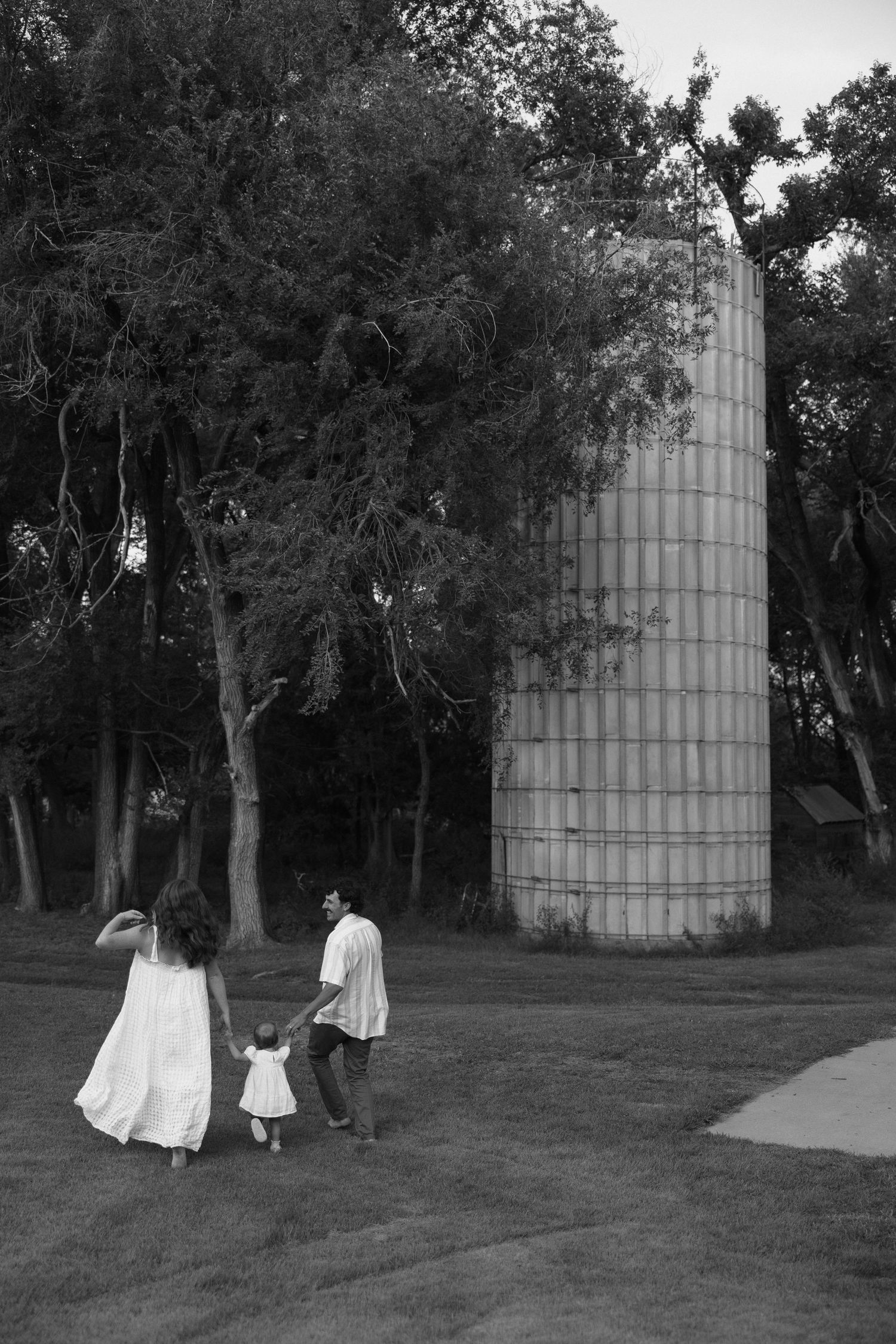 Family walking near a tall grain silo in black and white.