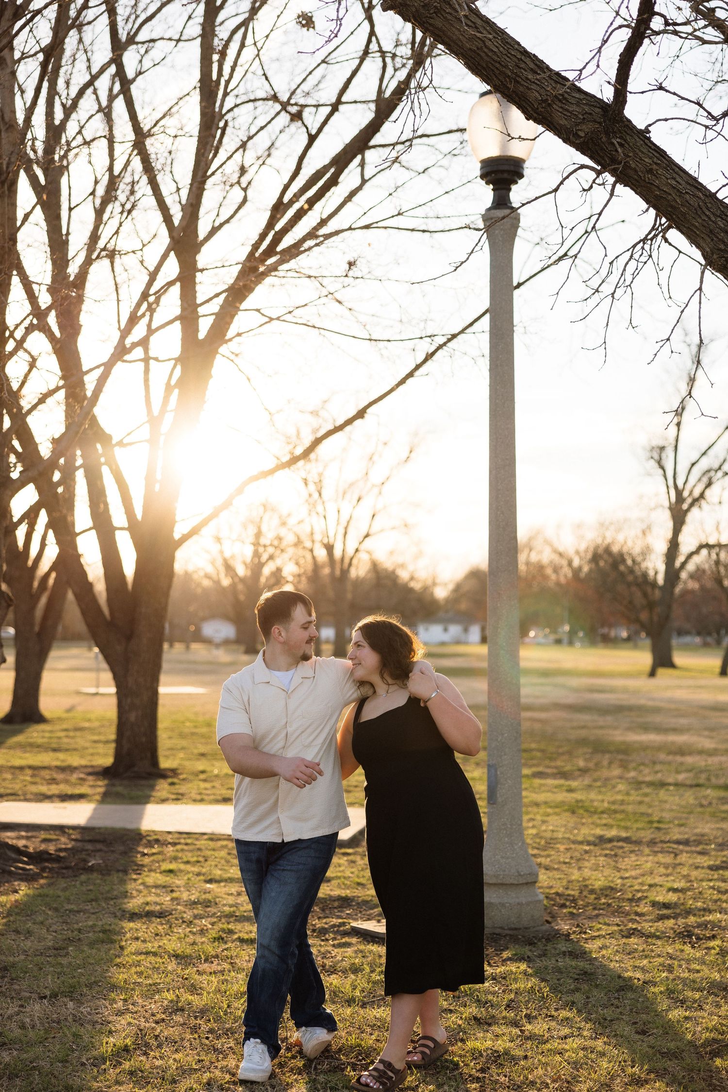 Couple sharing a romantic moment at sunset in a park with bare trees in the background.
