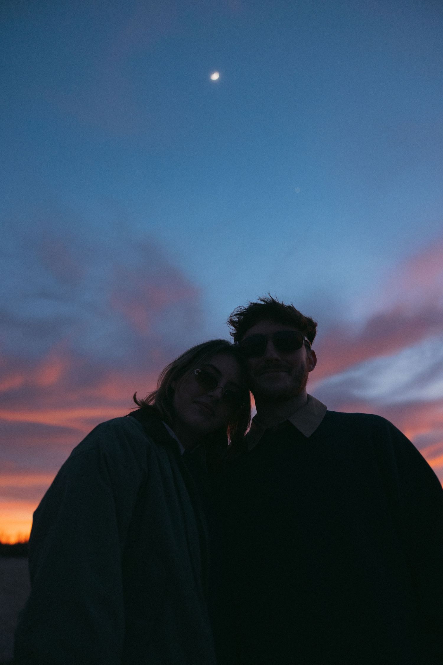 Silhouettes embrace against a dramatic sunset with deep blue and pink sky.