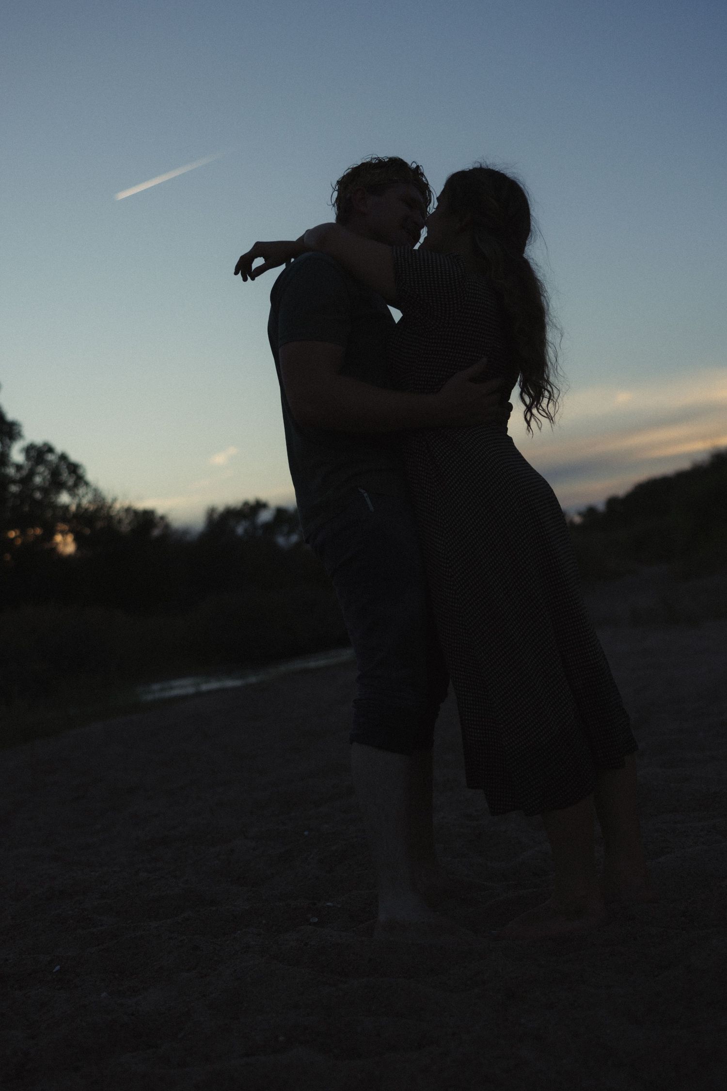 Silhouette of a romantic couple embracing and kissing at dusk outdoors.