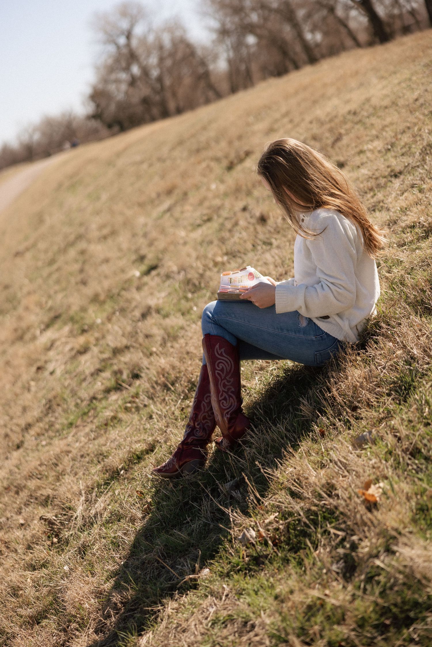 Person in white sweater sitting on grassy hillside during autumn.