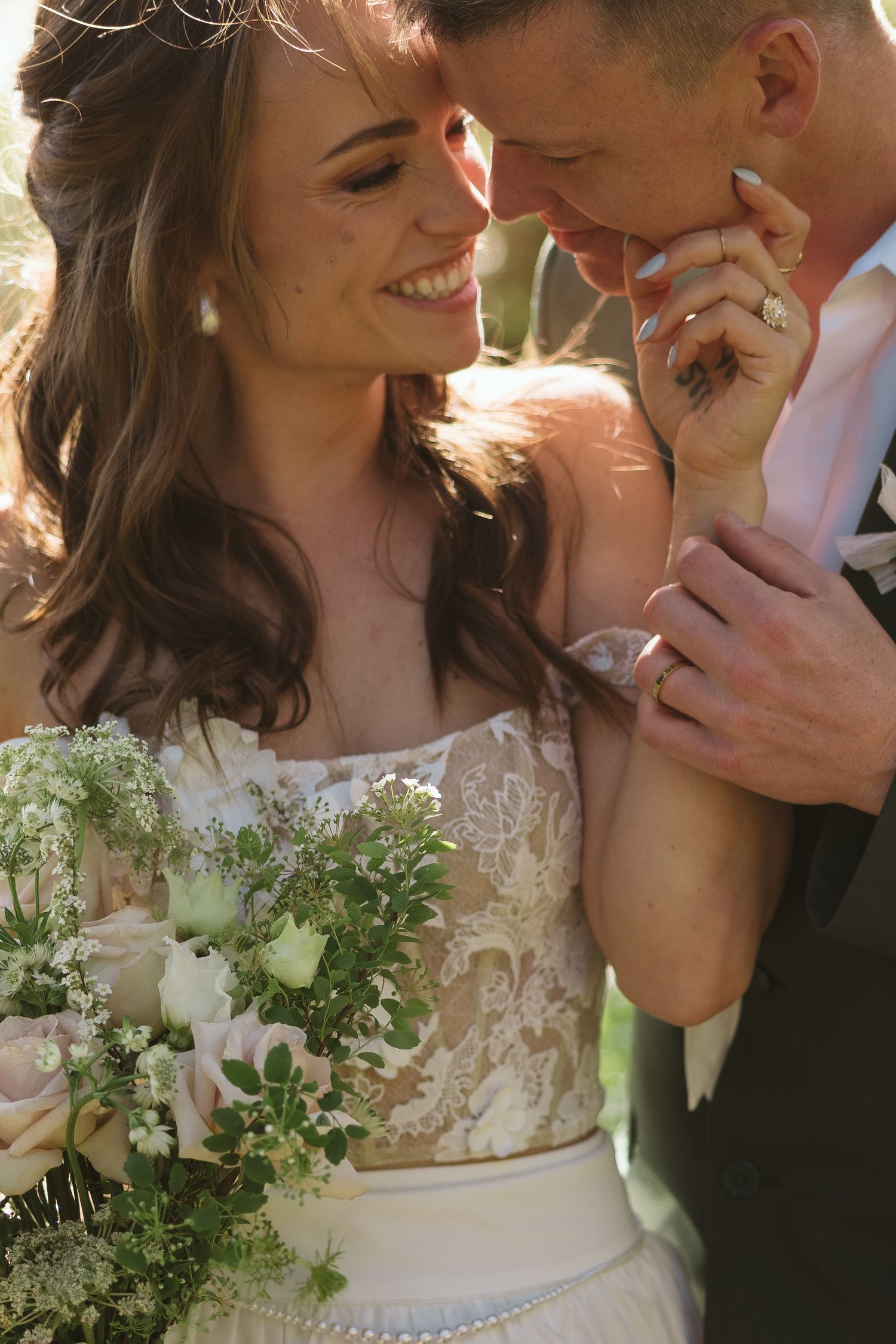 Intimate wedding portrait with white floral bouquet in natural sunlight.
