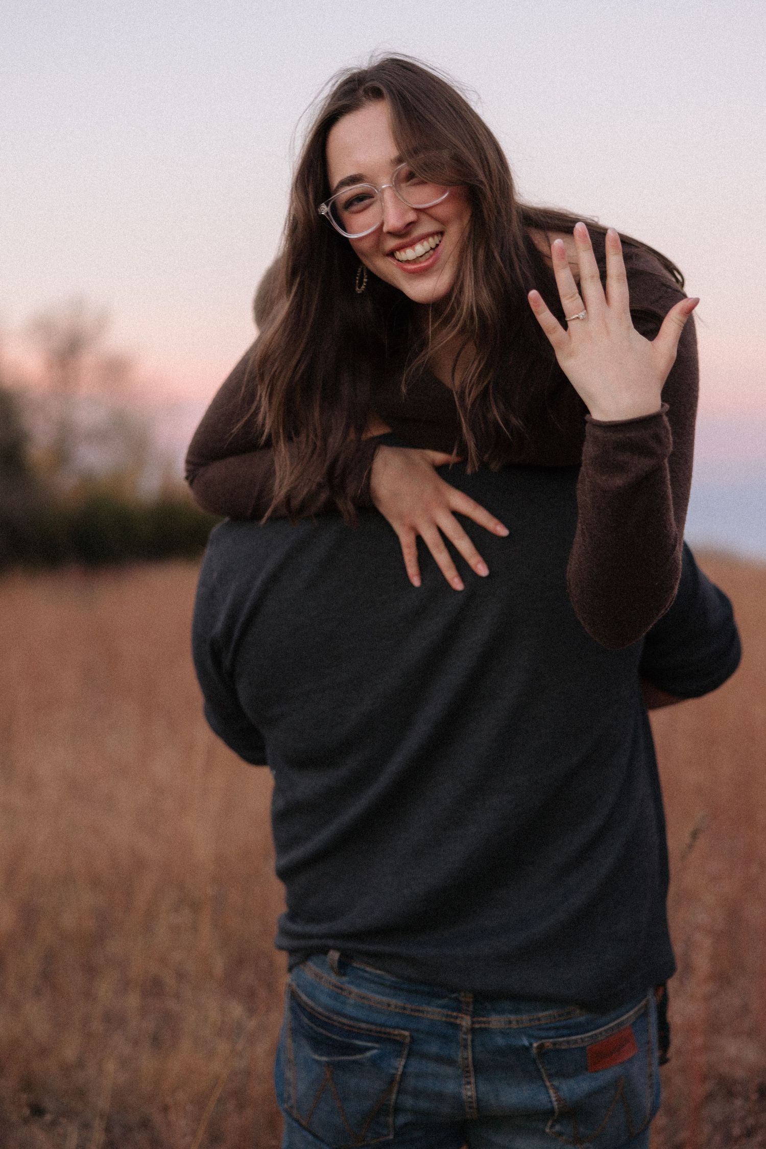 Person in dark sweater laughing and playing in autumn field at sunset.
