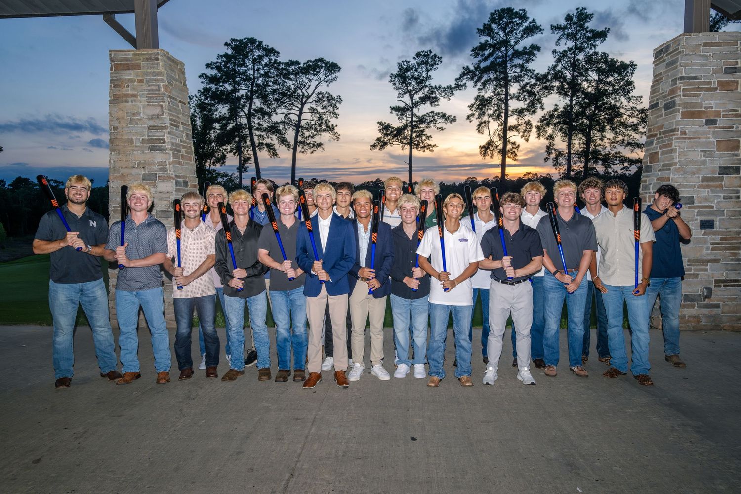 Group of students and adults pose outdoors at sunset holding awards at a ceremony.