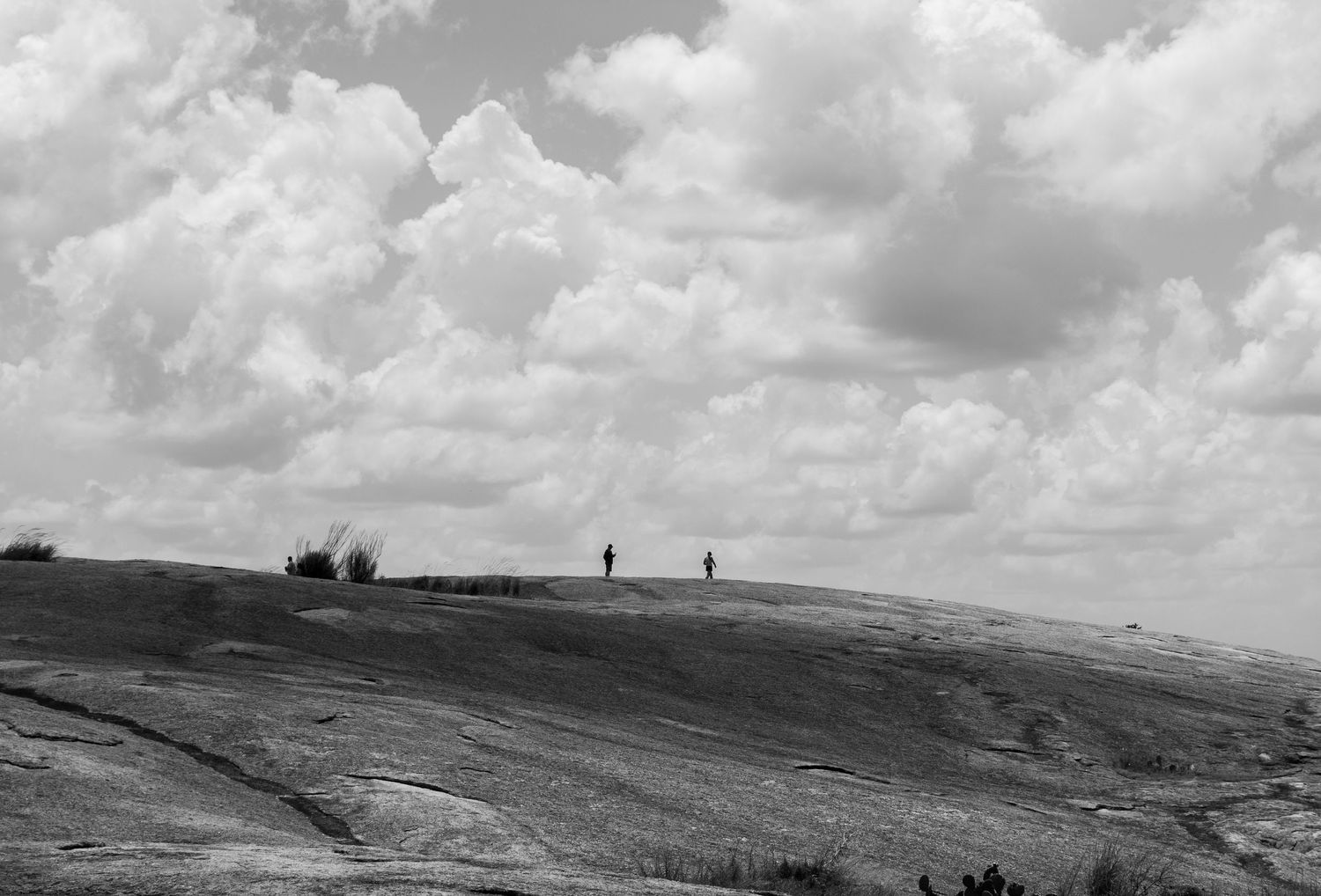 Two figures stand atop a vast rocky landscape under a dramatic cloudy sky in black and white.